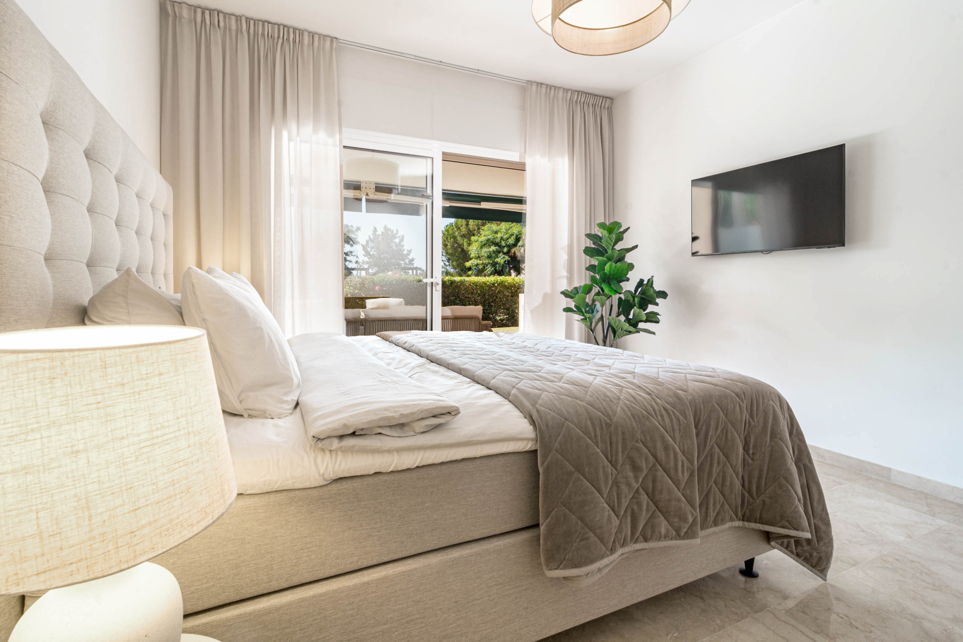 Bedroom with a mounted television on a white wall, a bed, and sliding glass doors to a patio.