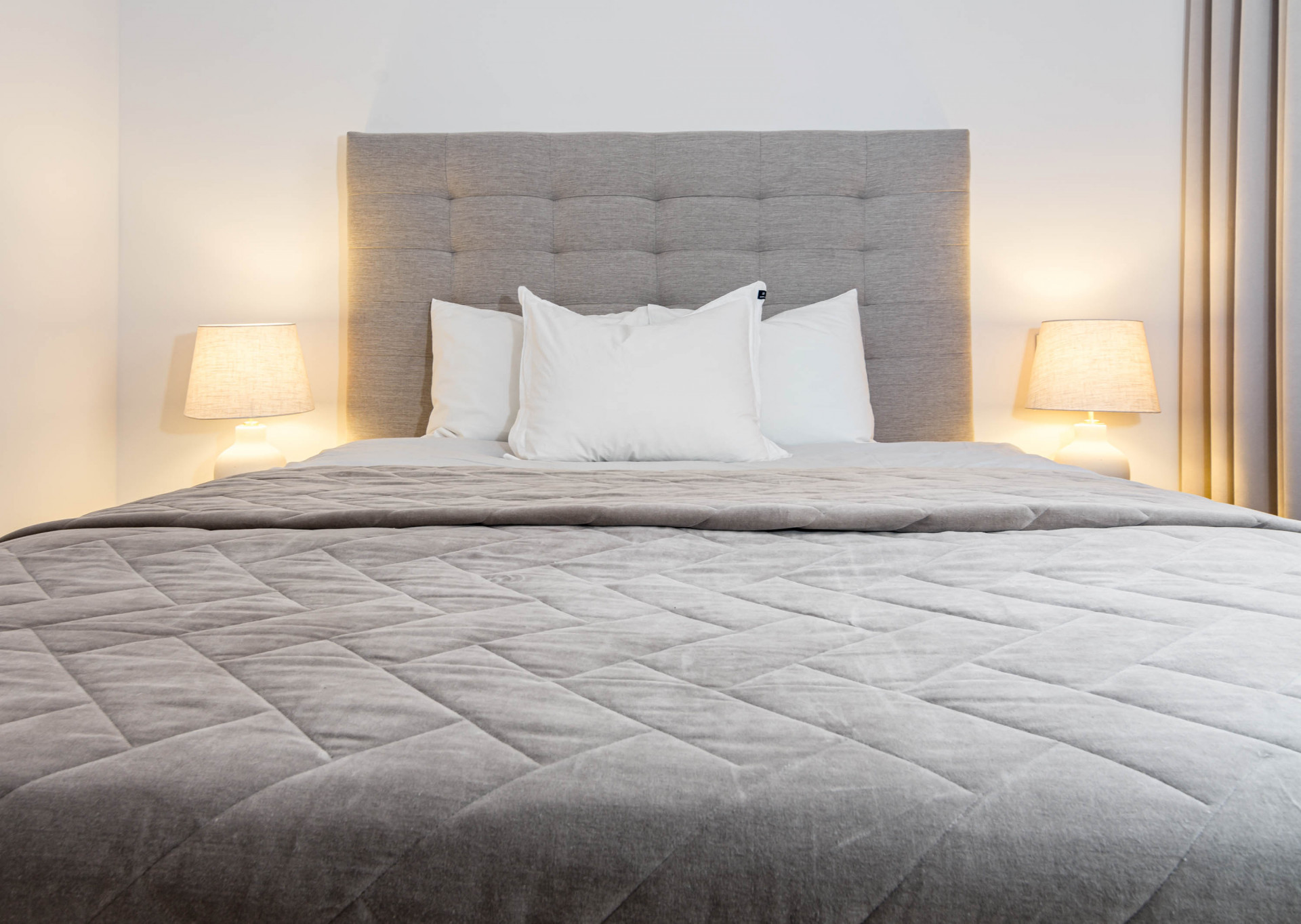 Close up of a bed with a gray upholstered headboard, white pillows, and a gray quilted comforter.