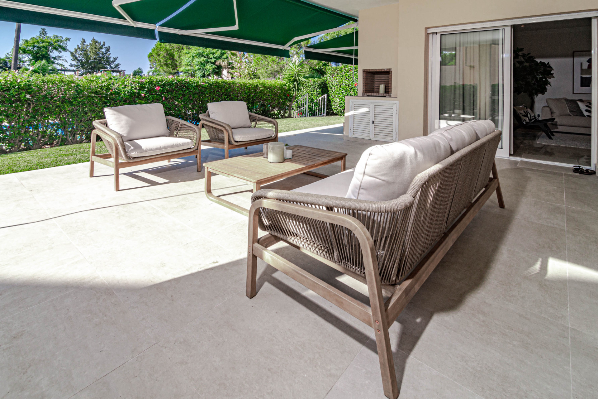 Angled view of an outdoor patio, two armchairs, a sofa, coffee table, and sliding glass door.
