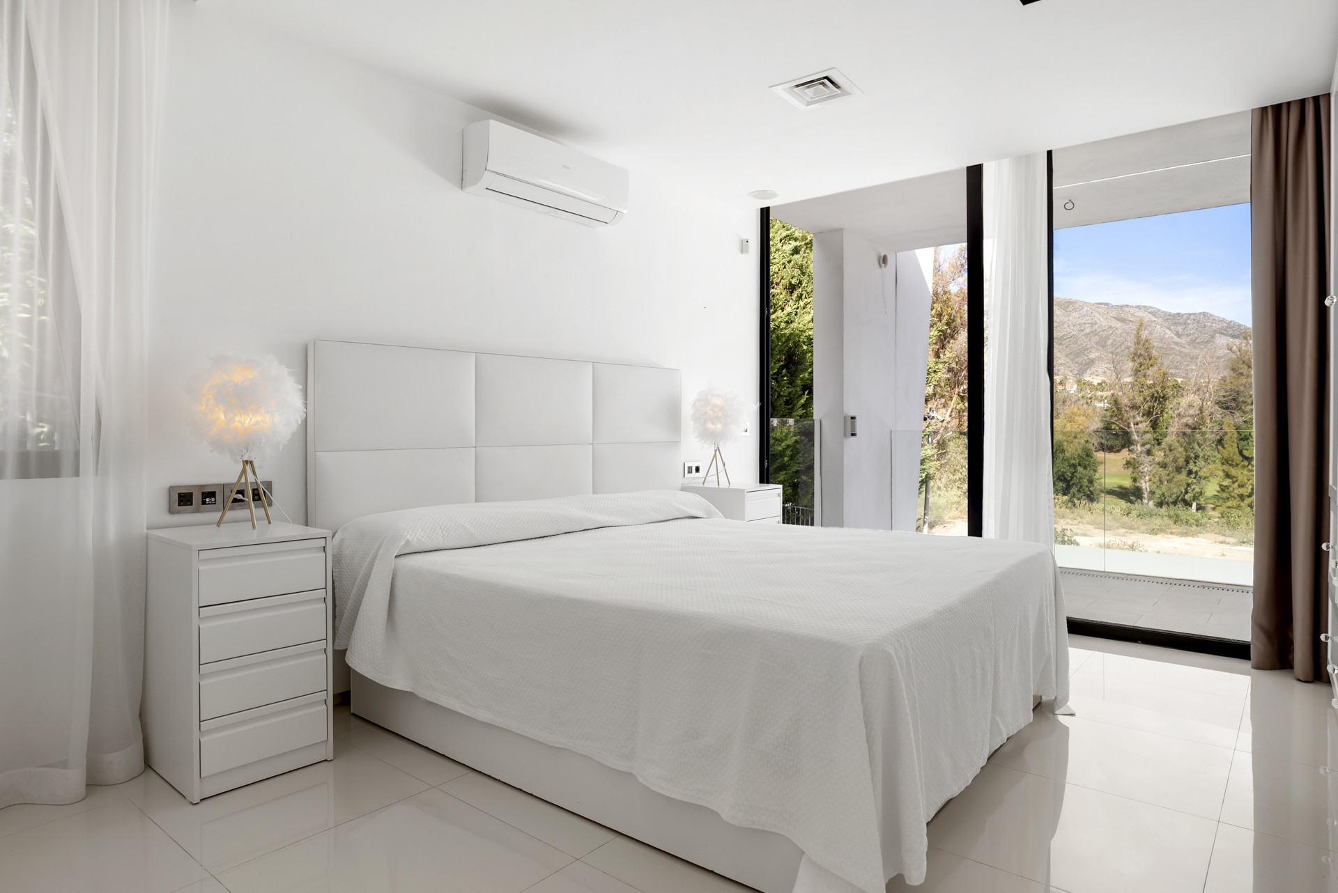 Bright bedroom featuring a white bed, modern decor, and large windows with mountain views.