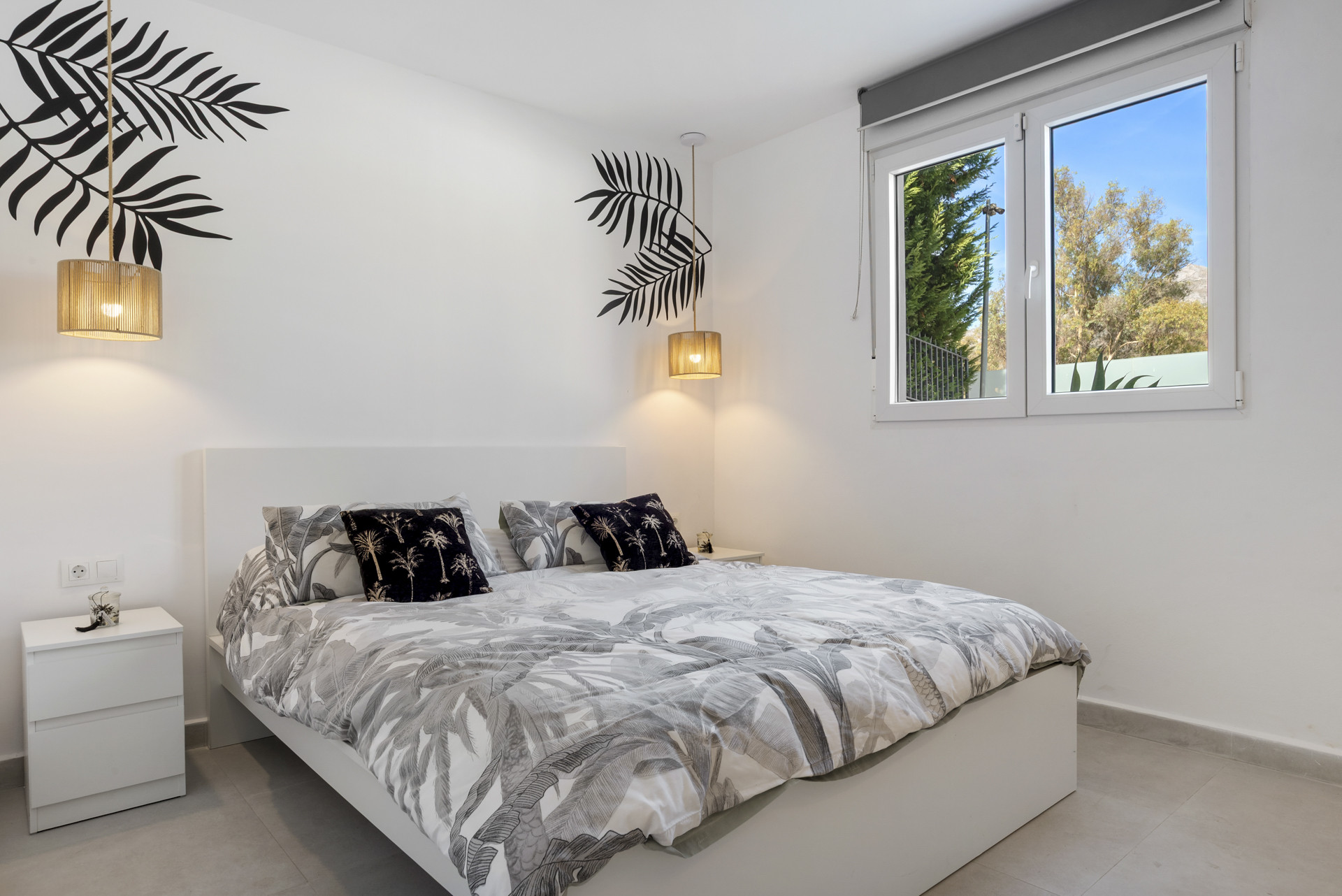 Bright bedroom with a queen-sized bed, decorative pillows, and large window with garden view.