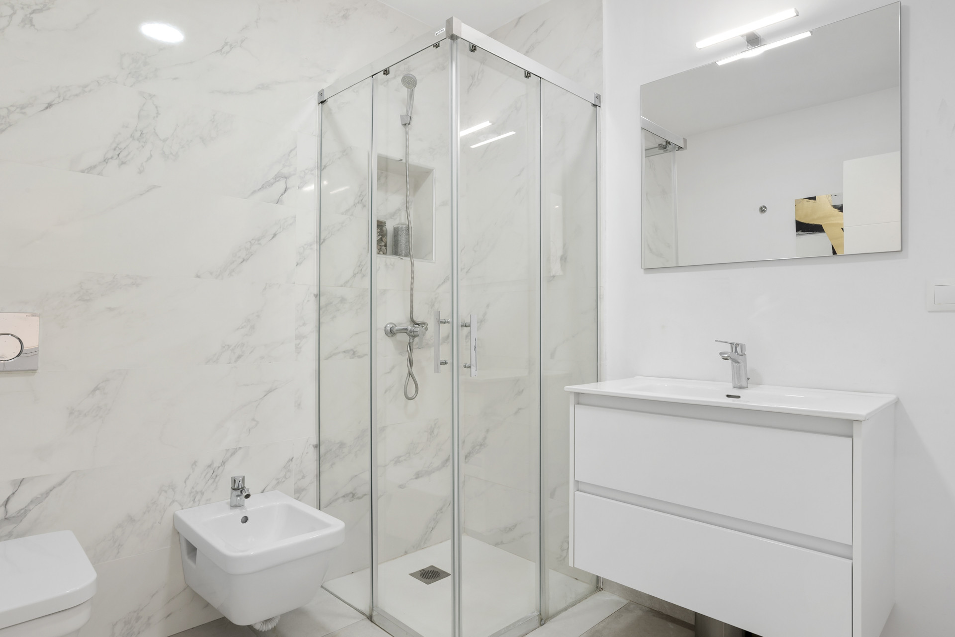 Modern bathroom with a glass shower, marble walls, sink with storage, and mirror above.