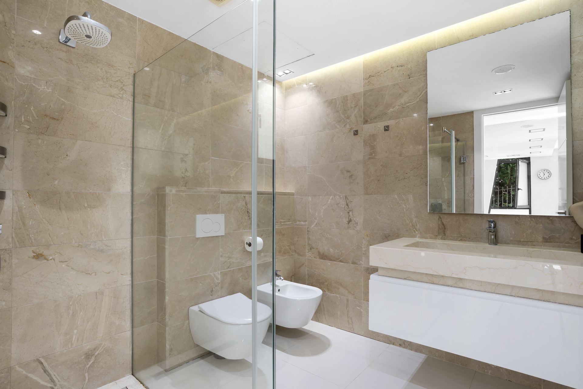 Elegant bathroom with a glass shower, bidet, and marble tiles.