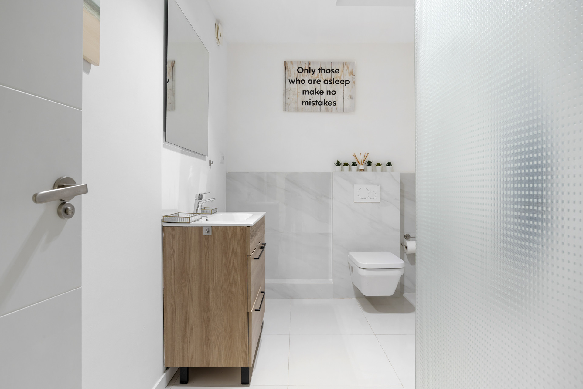 Bright bathroom with a wooden vanity, large mirror, and a wall-mounted toilet.
