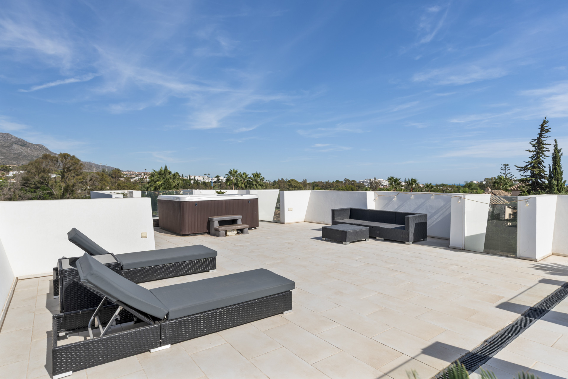 Rooftop patio with loungers, hot tub, and seating area against clear blue sky.