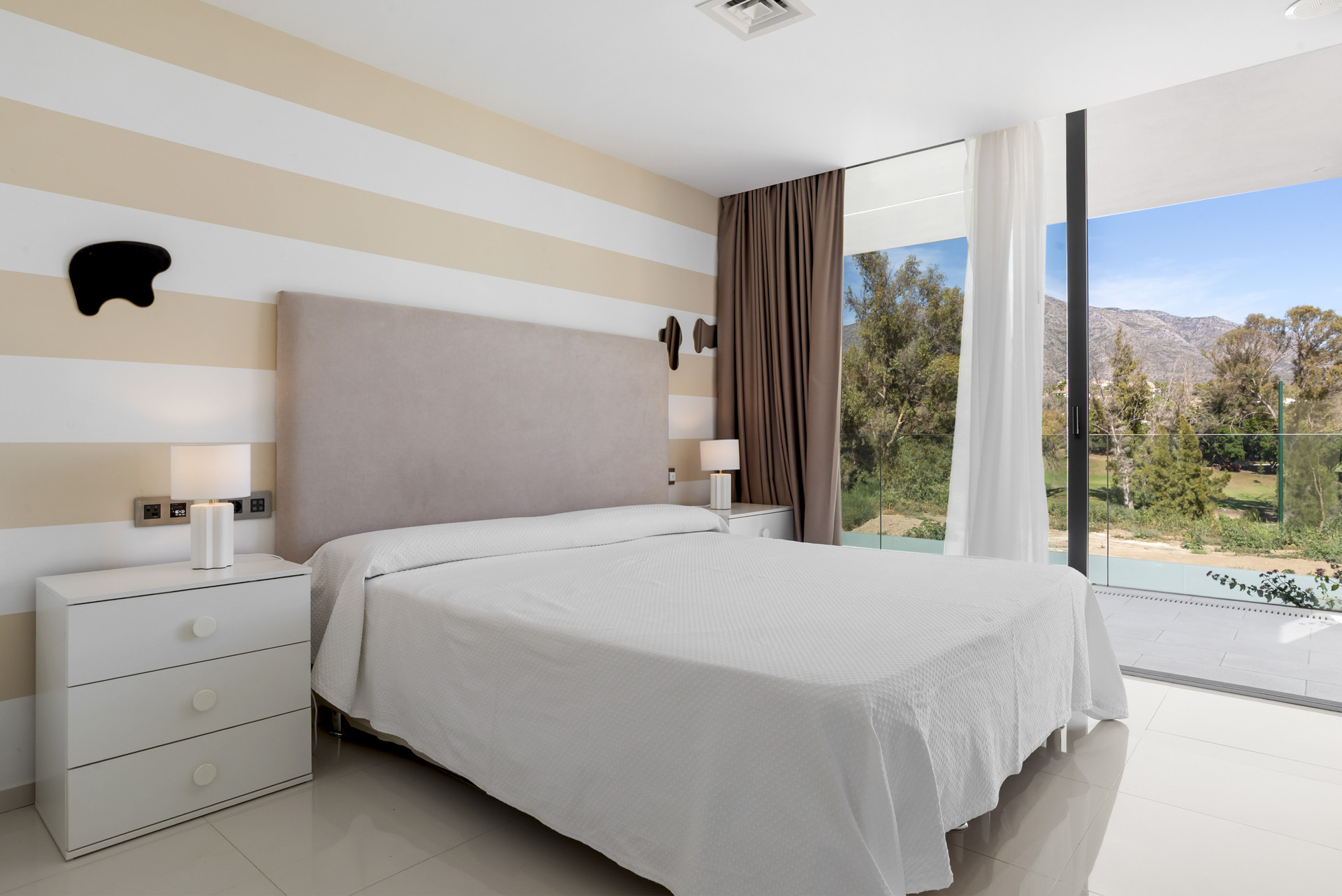 Serene bedroom with striped walls, a queen bed, and natural light from large windows.