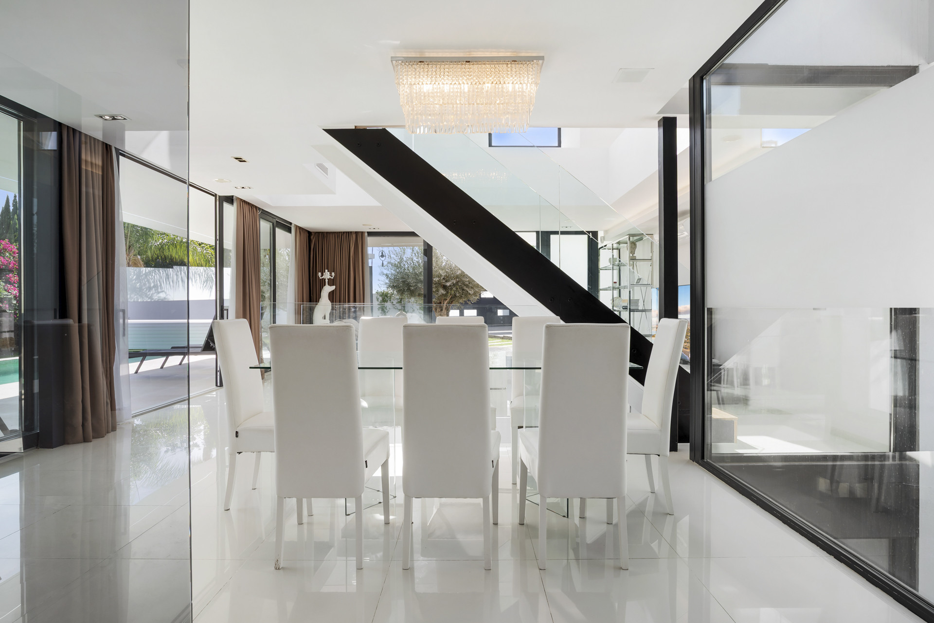 Dining room with a long table, white chairs, and clear lighting fixtures.