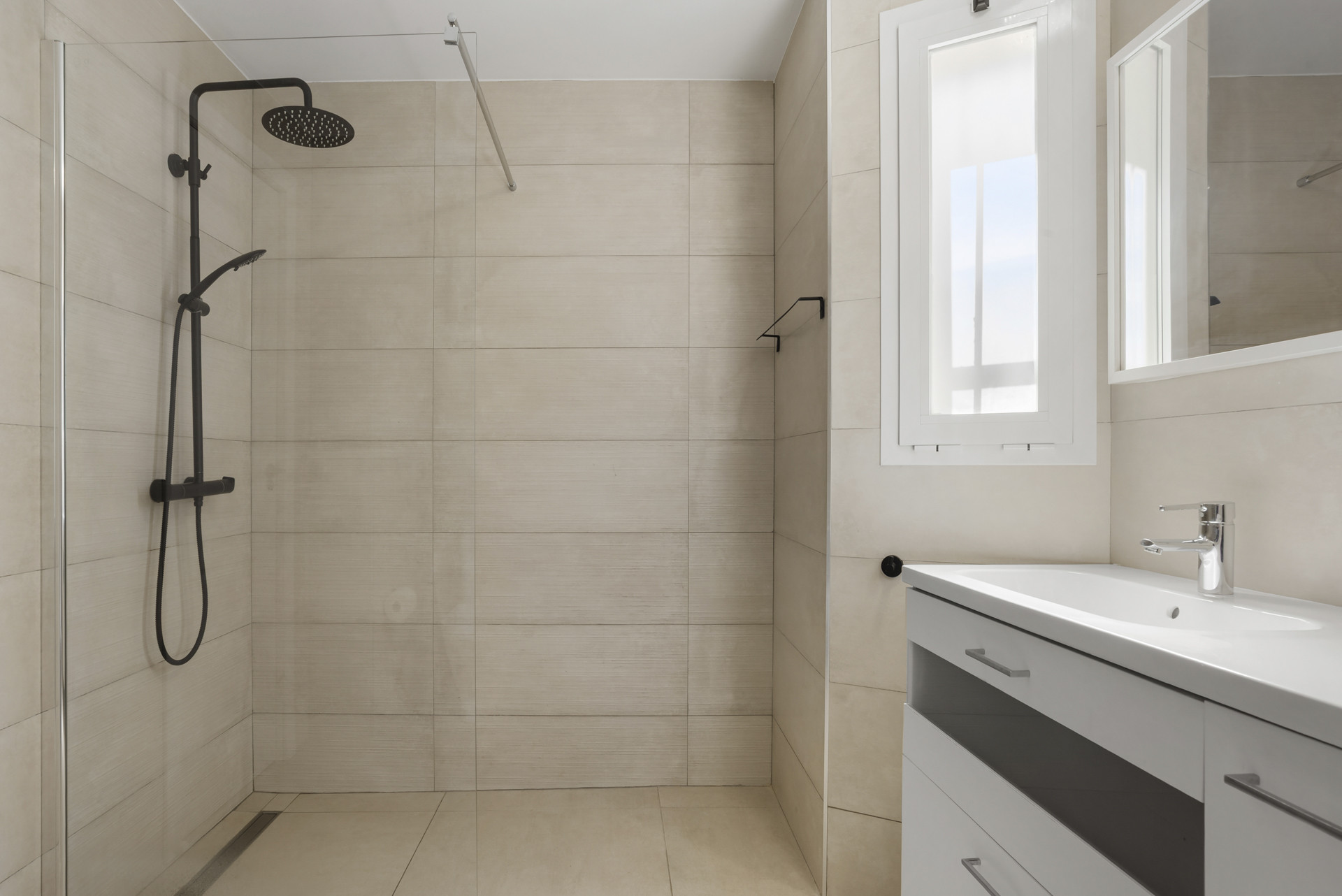 Bathroom with a walk-in shower featuring a black rainfall showerhead and a white vanity.