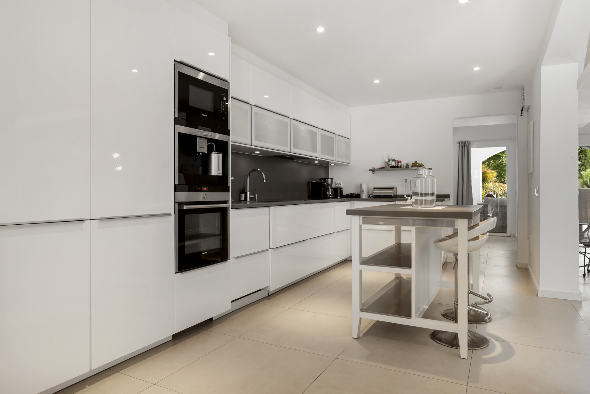Modern kitchen with white glossy cabinets, integrated appliances, and a central island with bar stools.