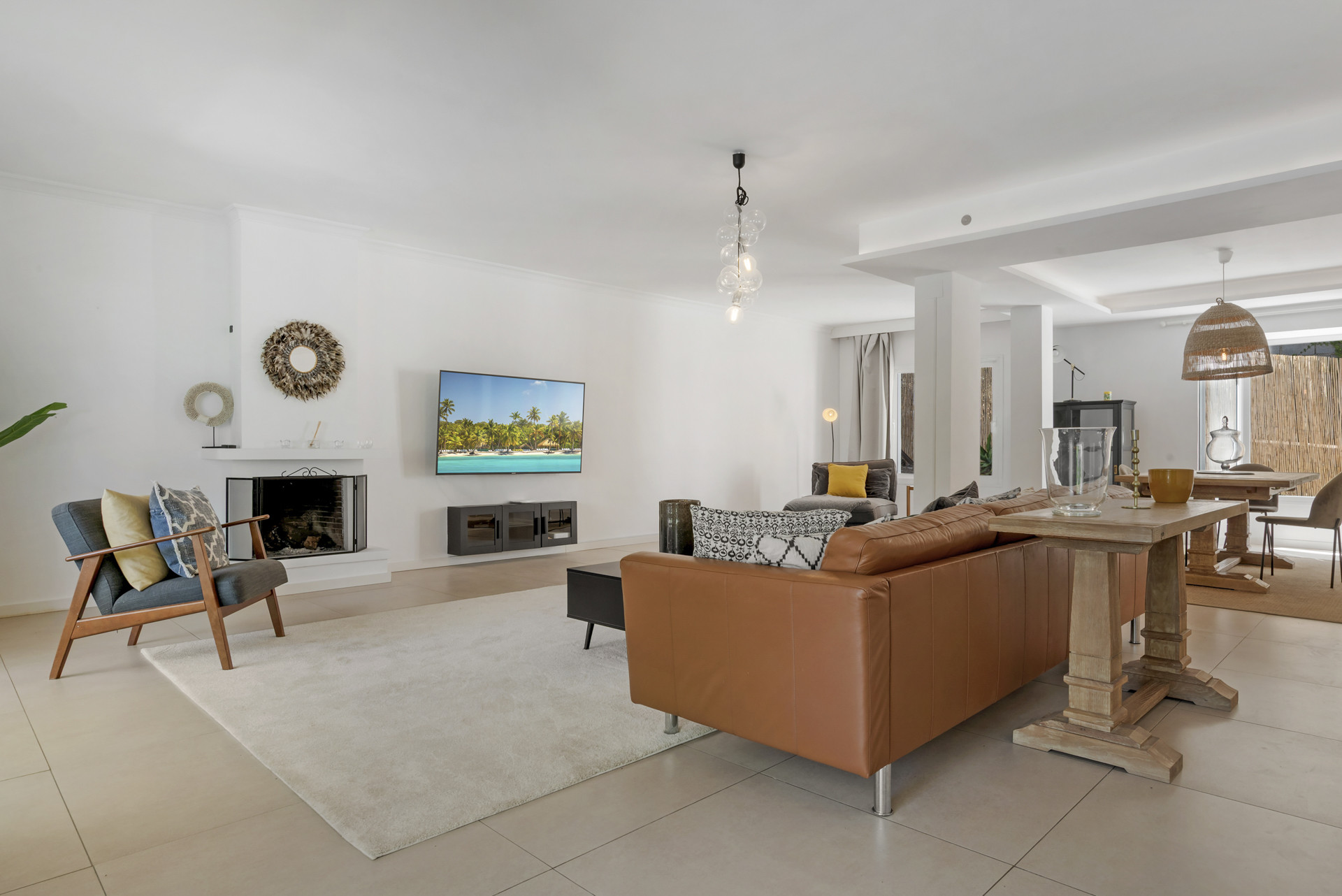 Spacious living area with a brown leather couch, fireplace, wall-mounted TV, and an adjacent dining space.