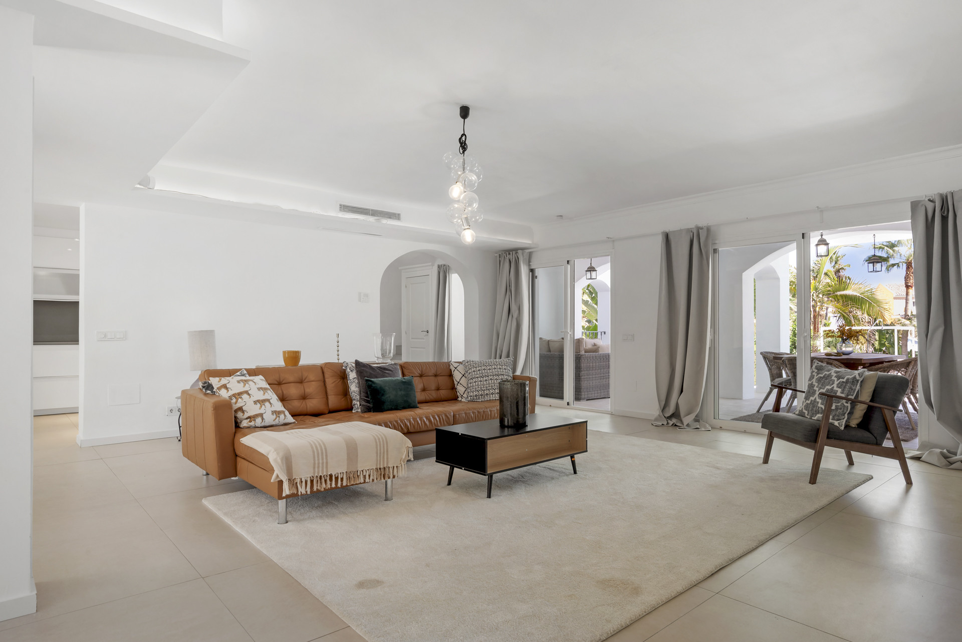 Bright living room with a large brown leather sofa, black coffee table, light rug, and sliding glass doors to patio.
