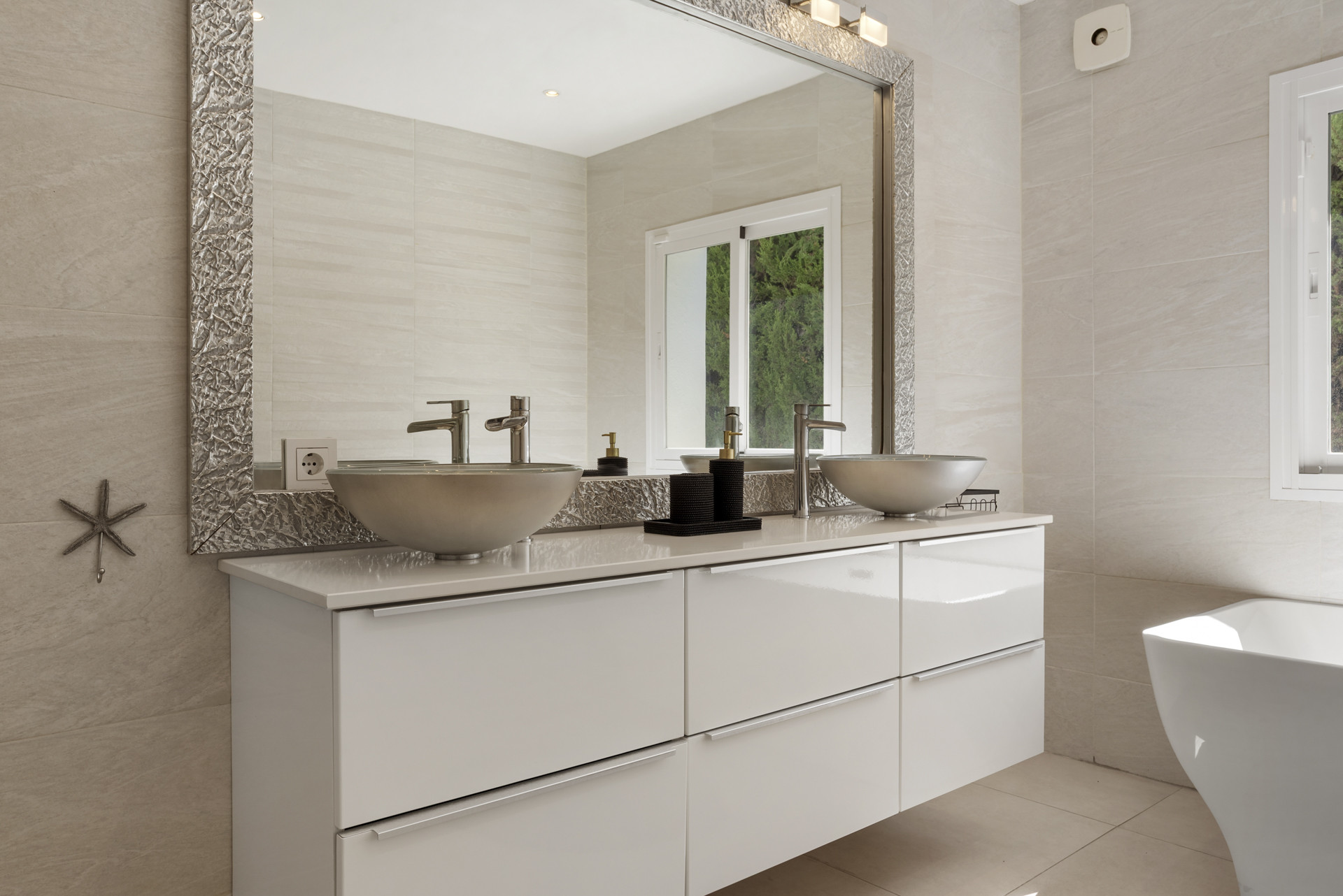 Bathroom vanity with two vessel sinks, large mirror, and window reflection showing a tub.