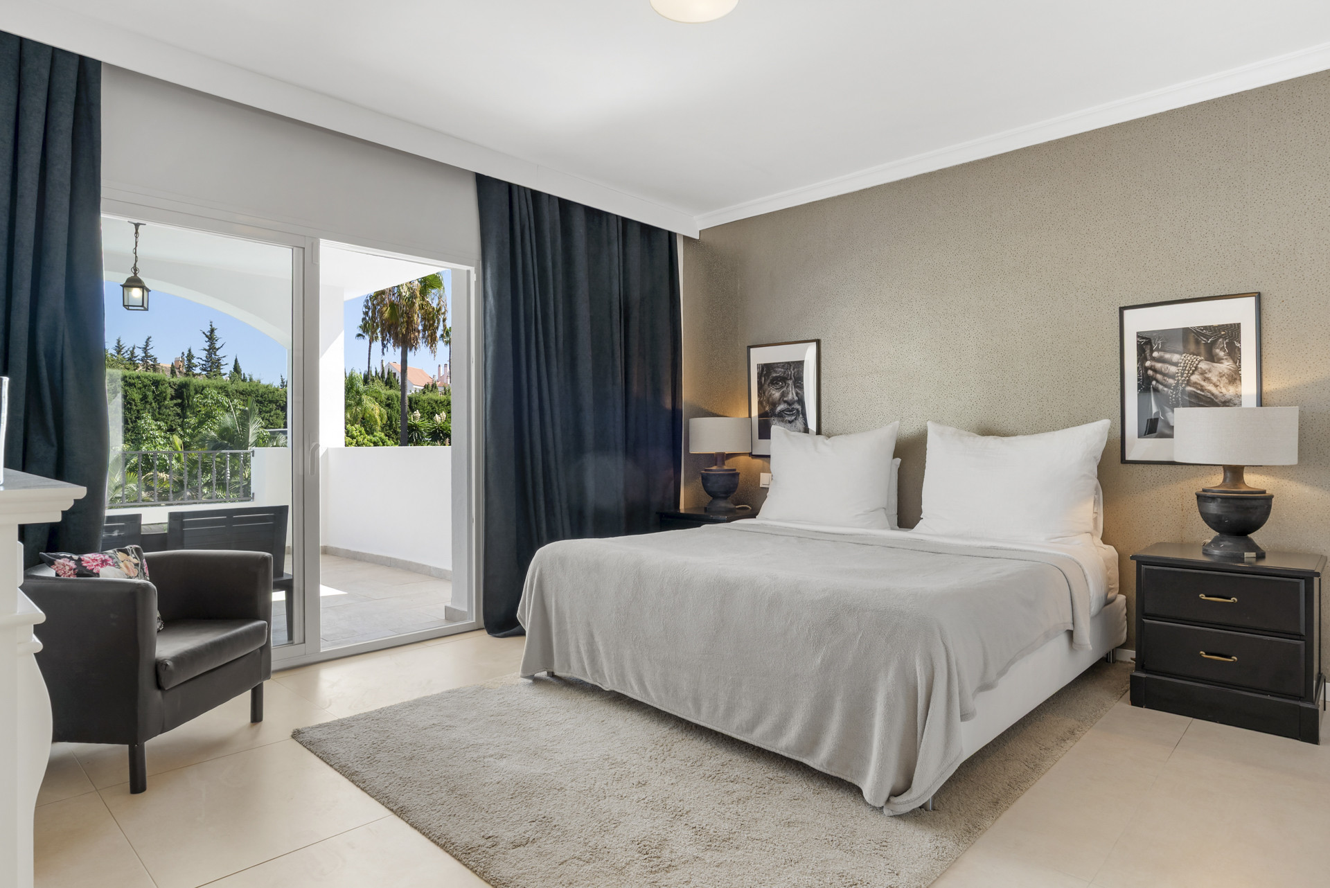 Bedroom with a bed, two nightstands, a grey armchair, and glass doors to a balcony.