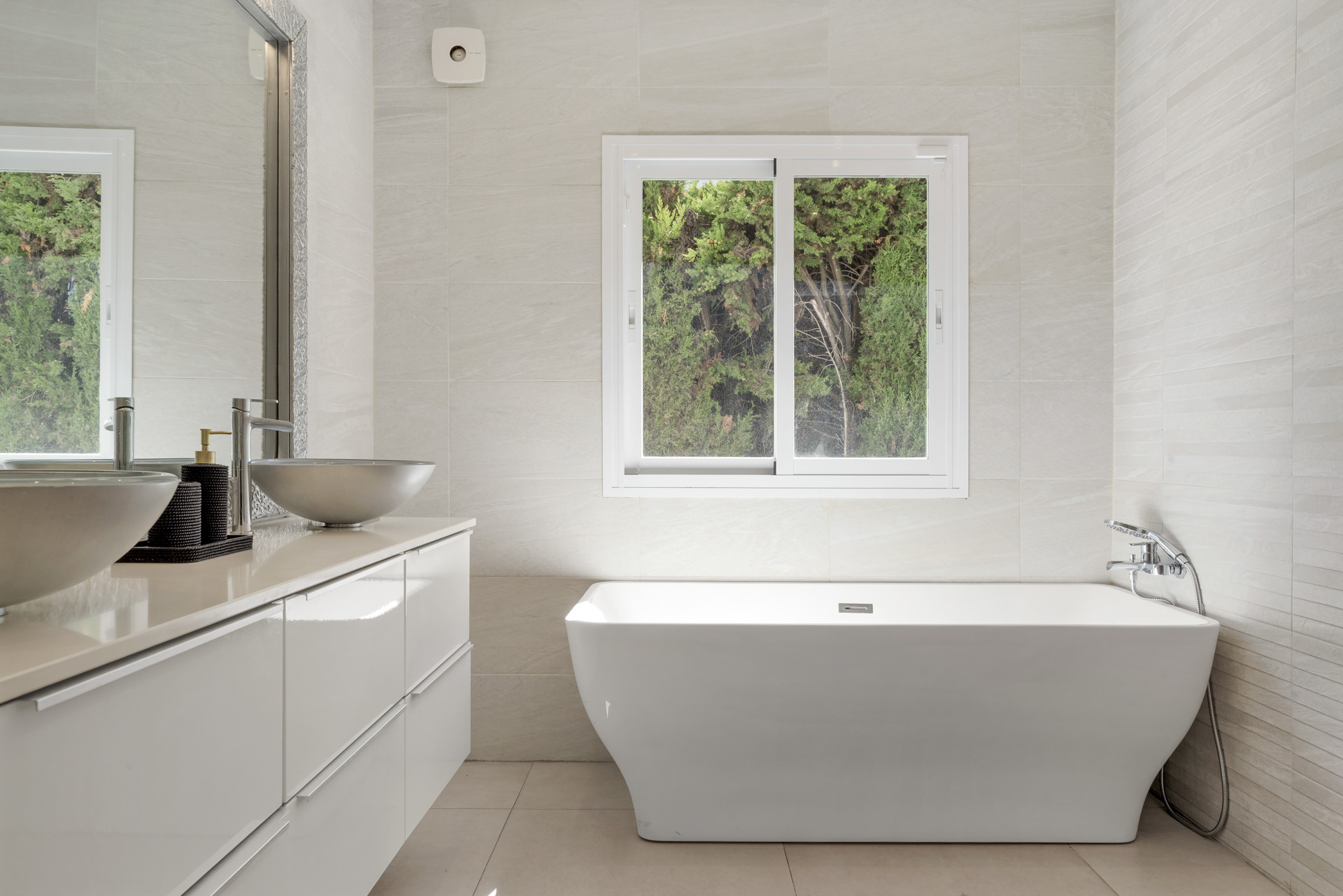 Bathroom with a freestanding tub, dual basin vanity, and a window overlooking greenery.