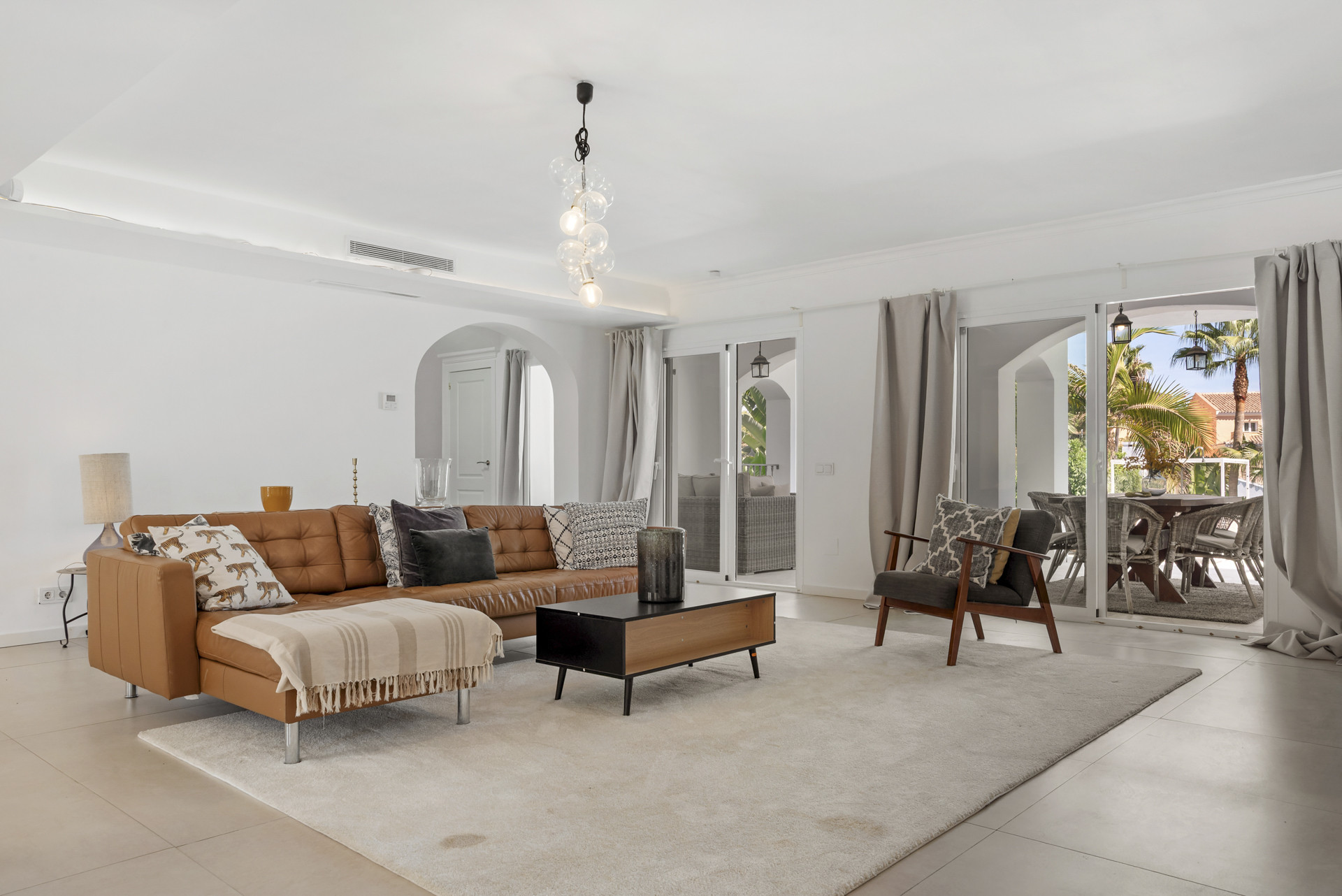 Living room with a large tan leather sofa, coffee table, white rug, and glass doors opening to a patio.