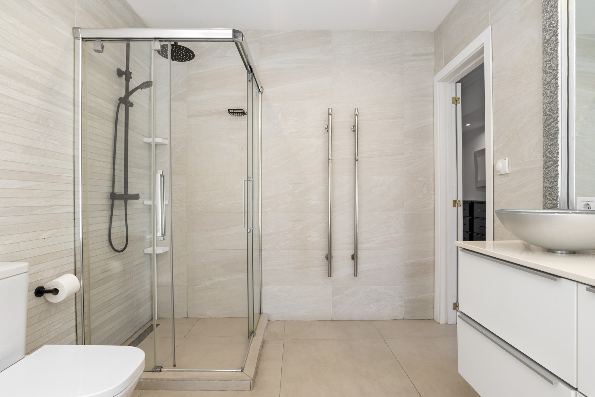 Bathroom with a glass enclosed shower, toilet, and towel warmers on a tiled wall.