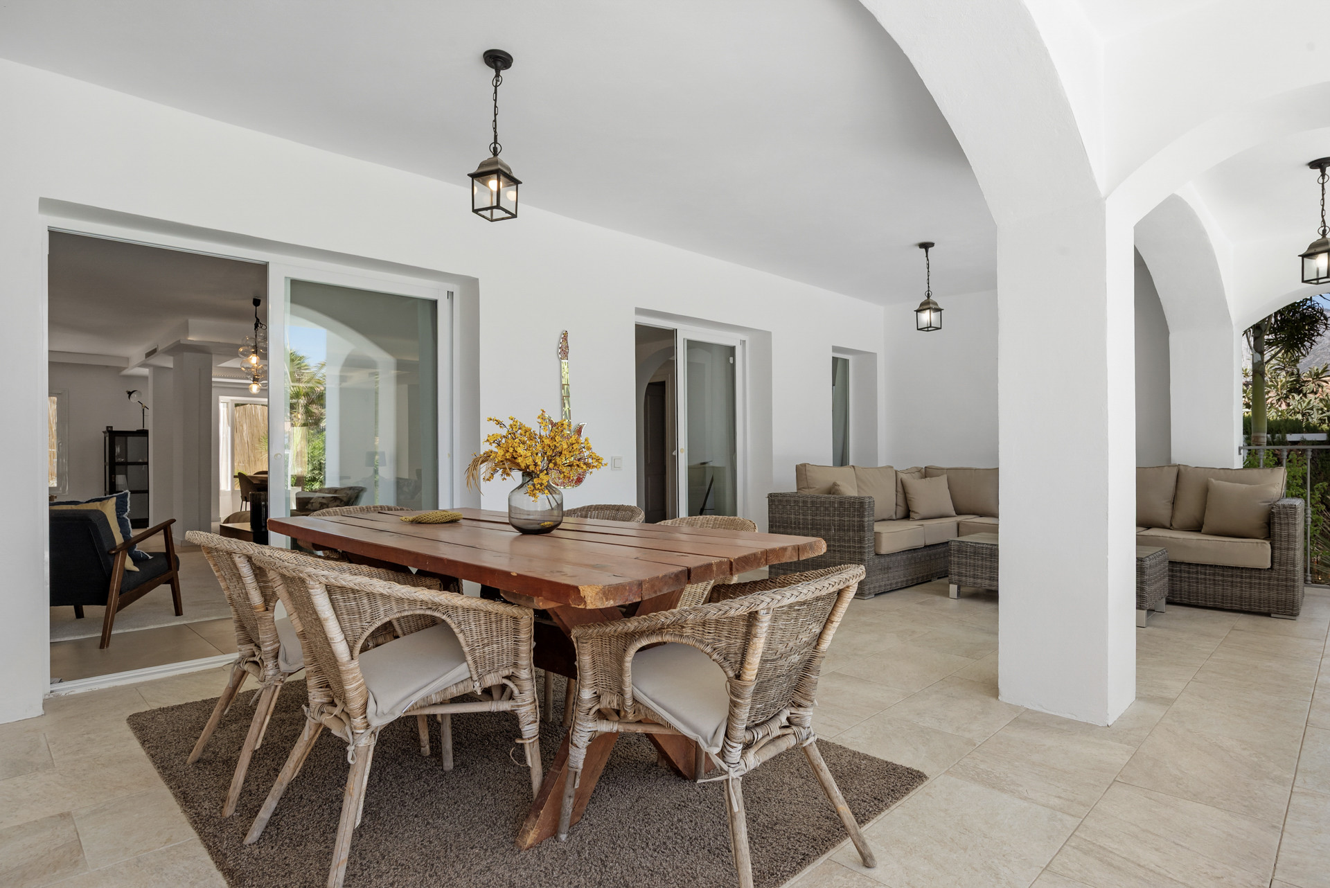 Covered patio with a wooden dining table, wicker chairs, and cushioned outdoor sofas.