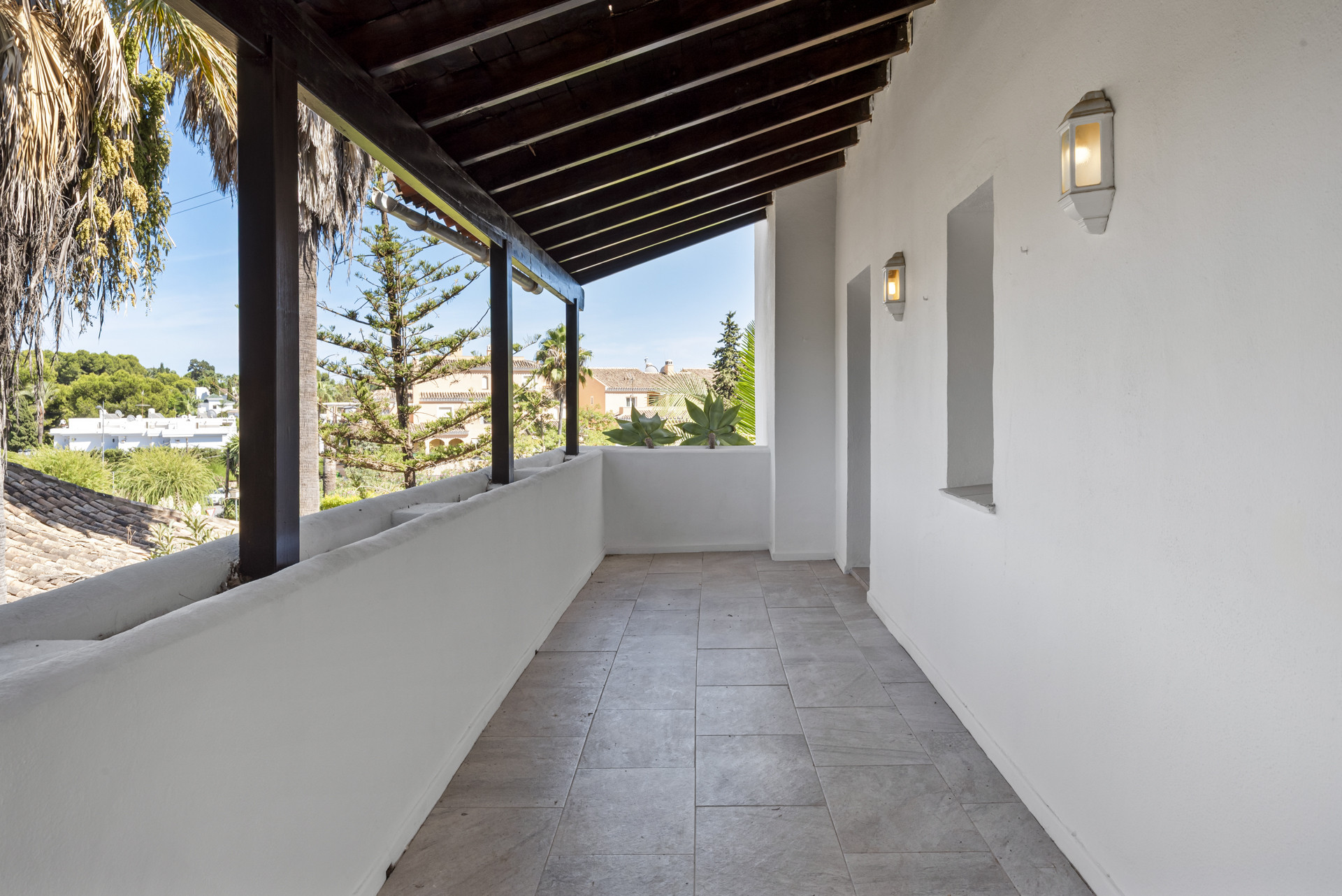 Long, narrow, covered balcony with tiled floor, white walls, and view of residential area.