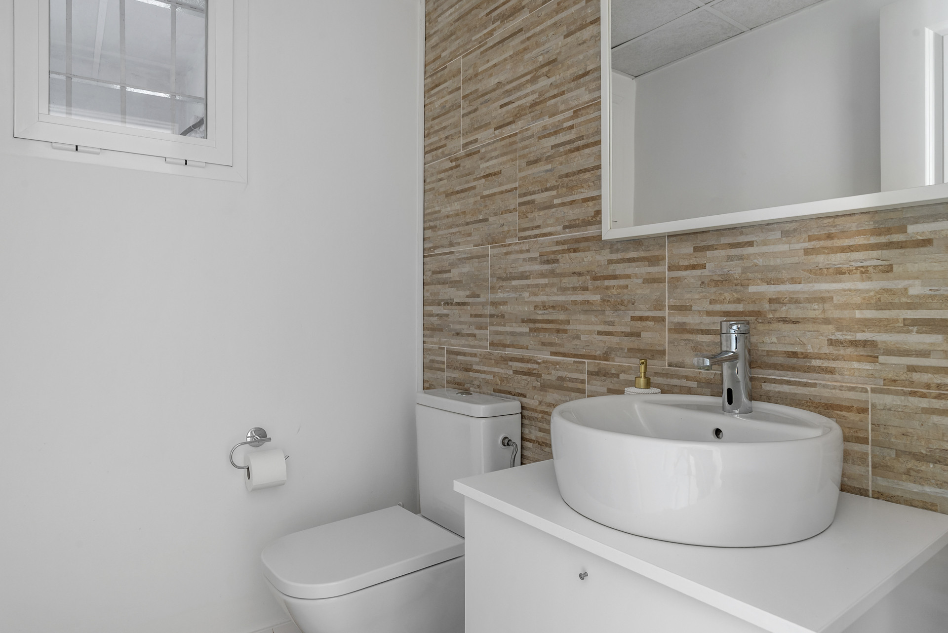 Bathroom with a white toilet, vessel sink on a vanity, and tiled accent wall.