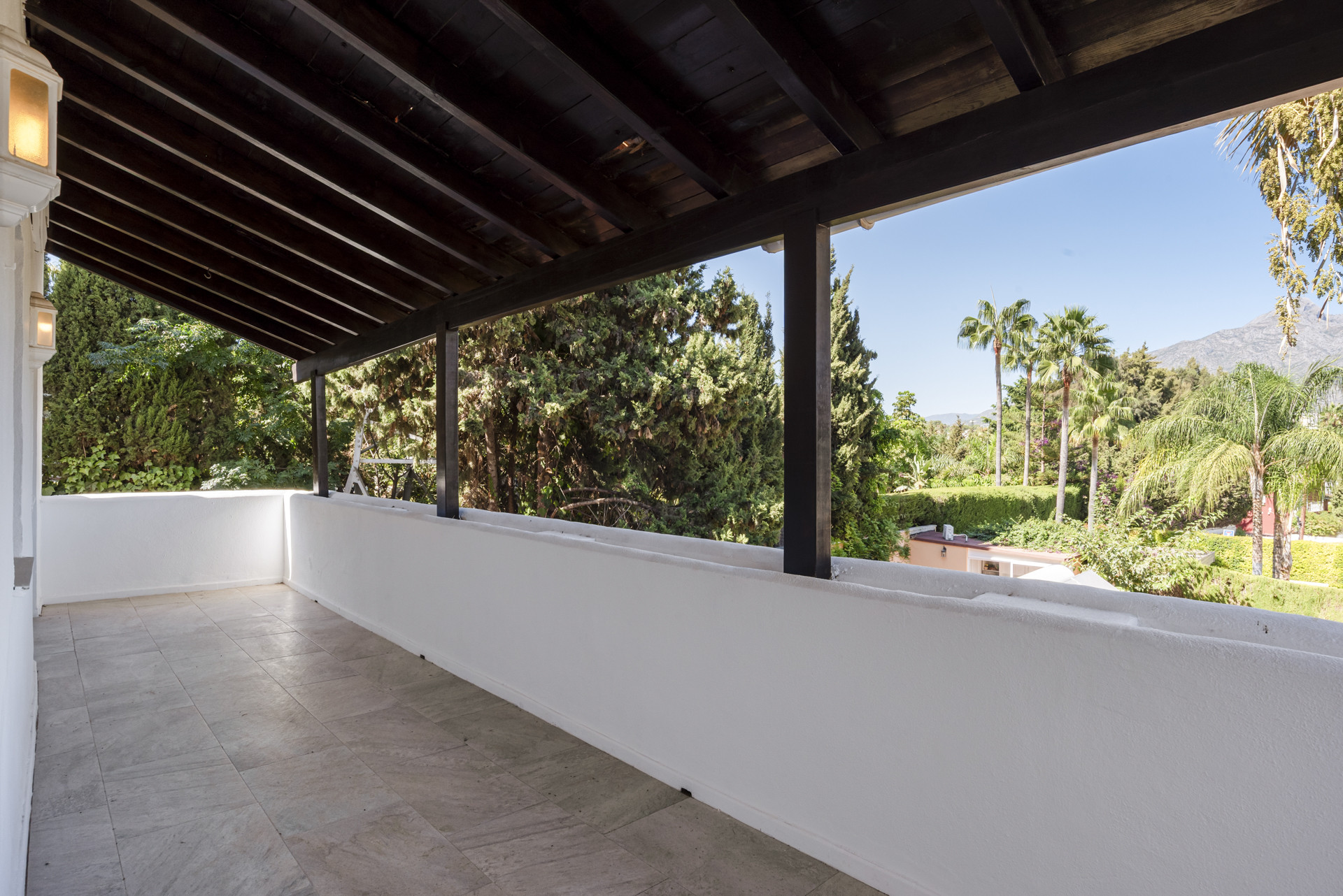 Outdoor covered patio with tiled floor, white wall, and a view of trees and distant mountains.
