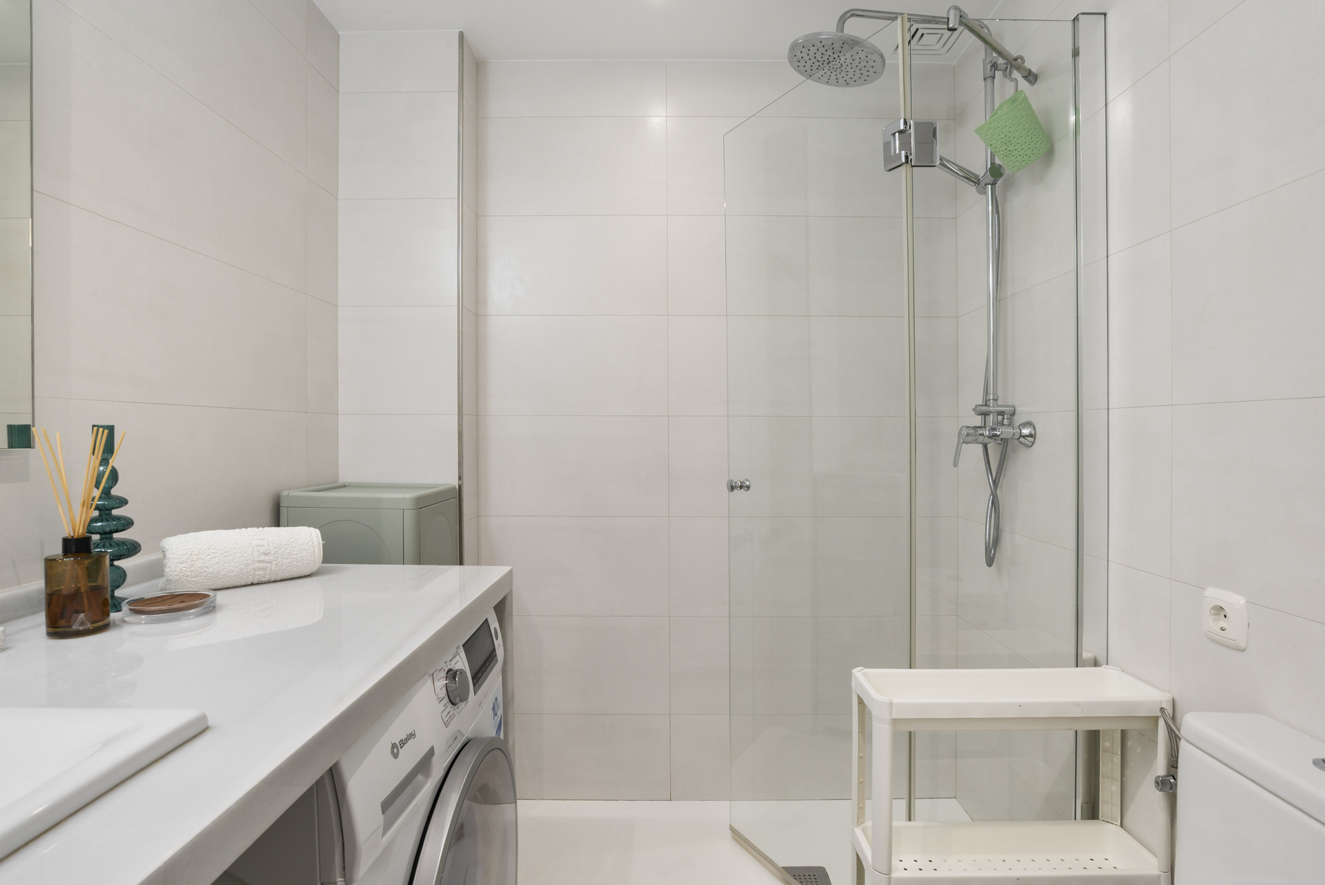 Compact bathroom with a shower, washing machine, and minimalistic decor.