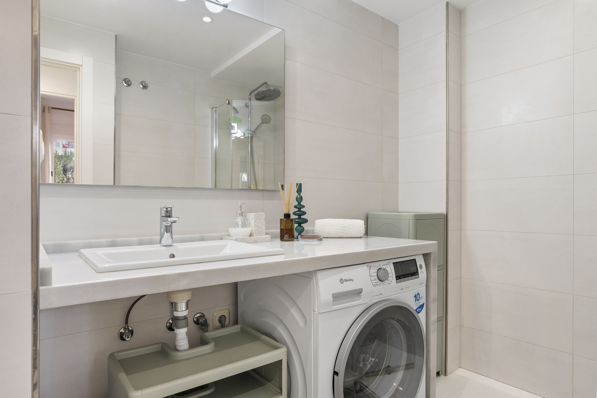 Modern bathroom with a washing machine, sink, and shower, featuring light-colored tiles.