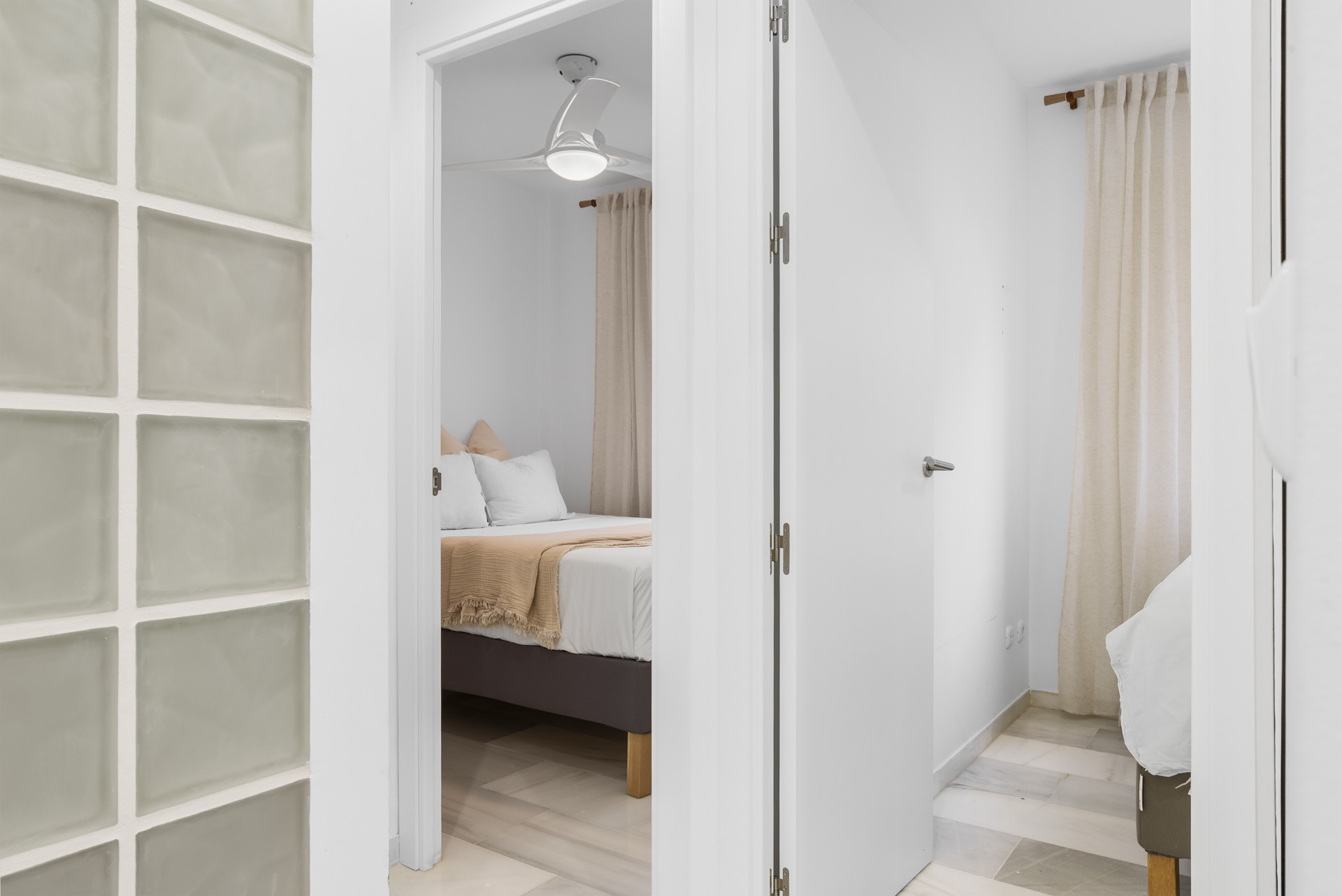 View of a bright corridor with a glass block wall leading to a bedroom.