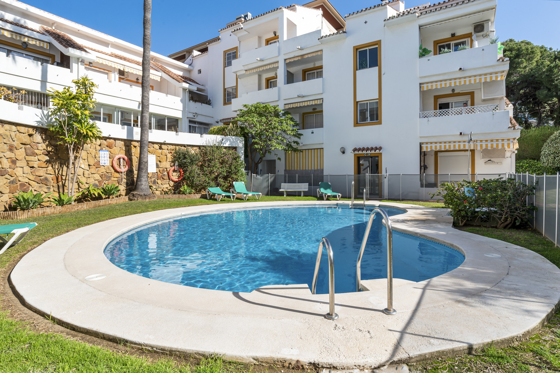 View of pool area with a stone wall and green landscaping.