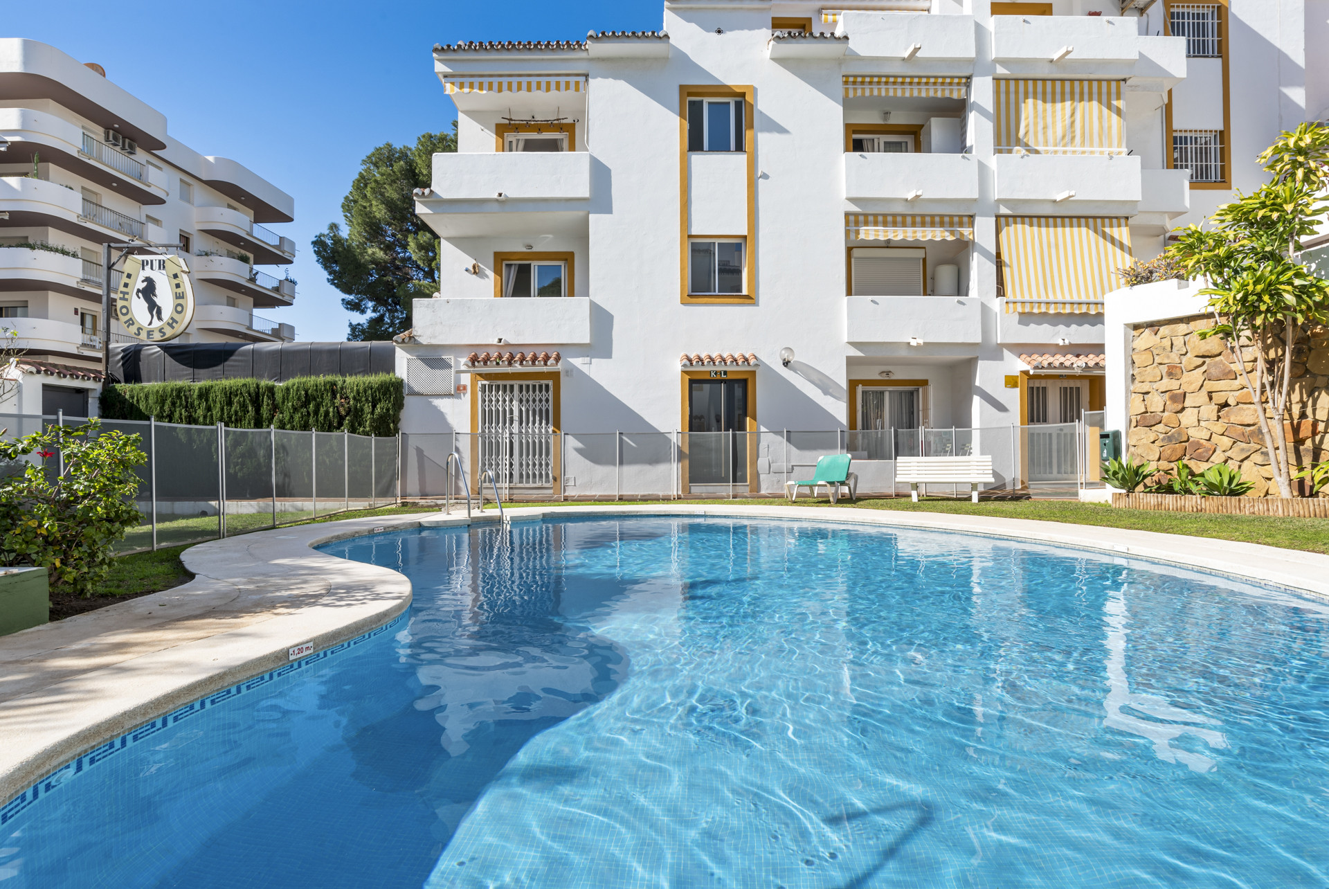 Swimming pool view with surrounding grass and white building.