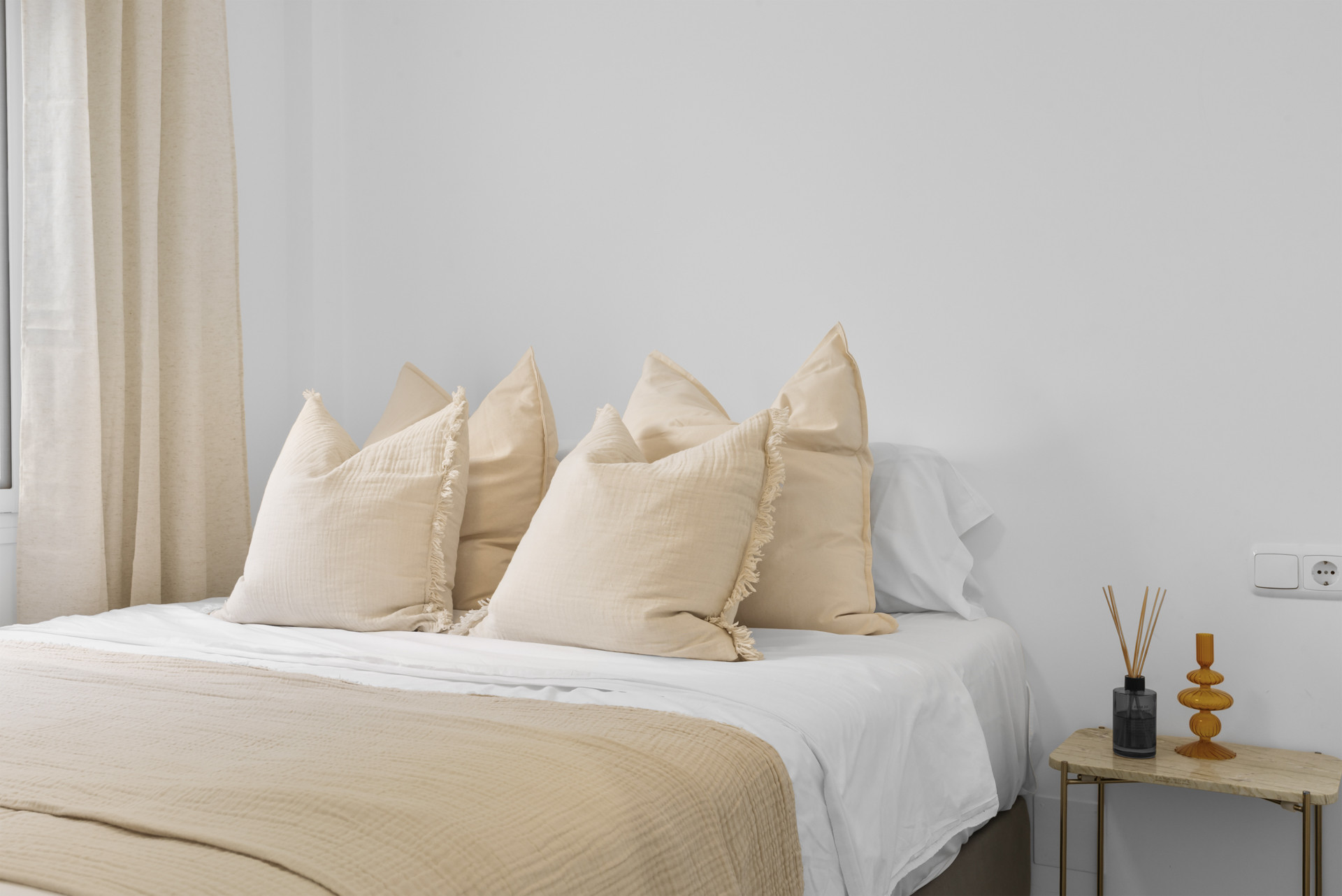 Close-up of a bed with beige decorative pillows and a small bedside table.