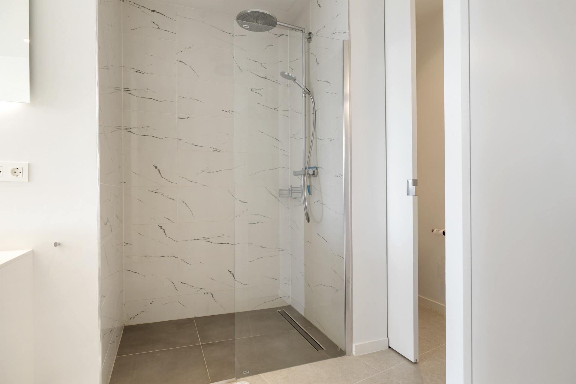 Contemporary walk-in shower with light marble-patterned tiles and a clear glass door.