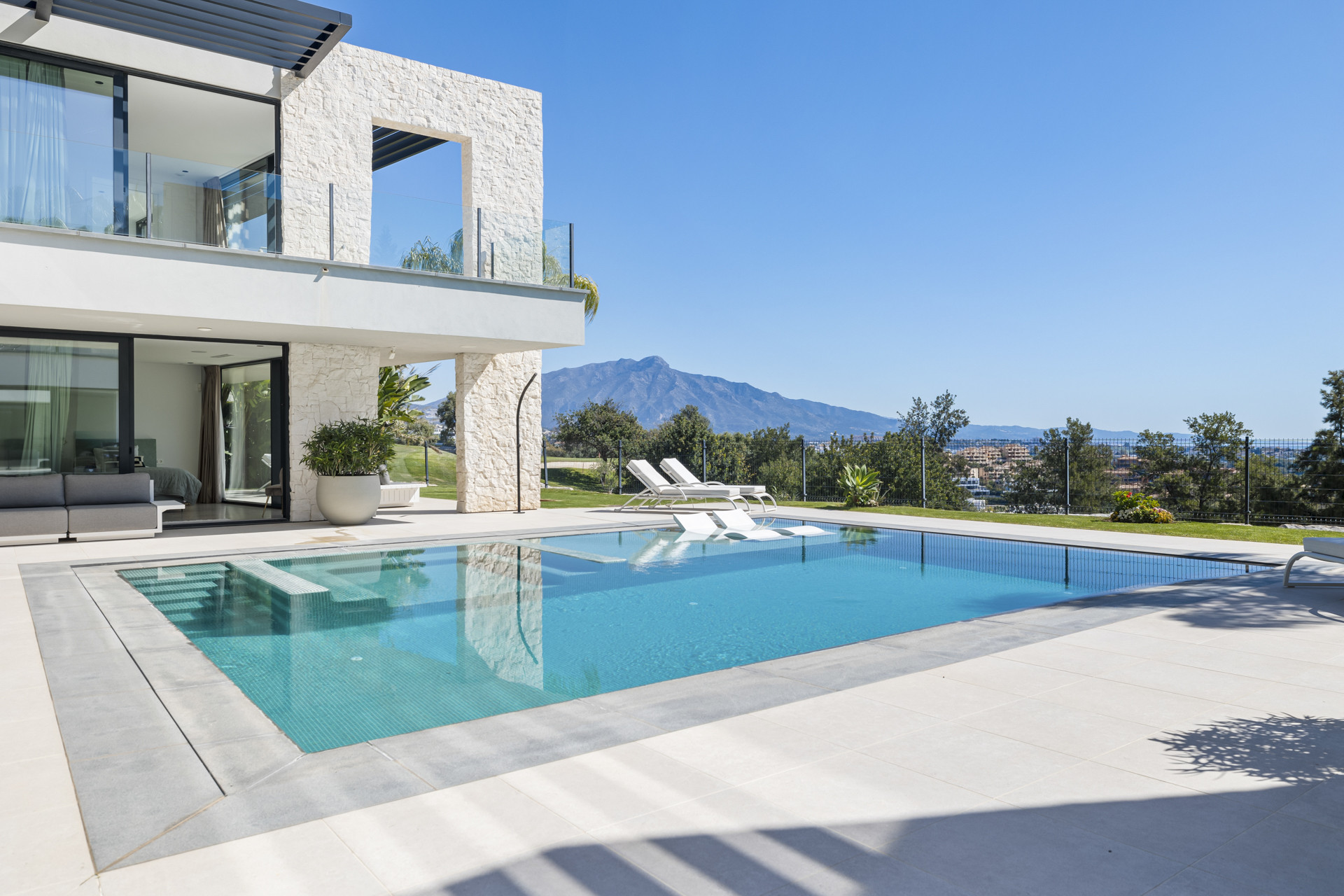 Exterior of a white modern house with a pool, mountains in the distance, and green landscaping.
