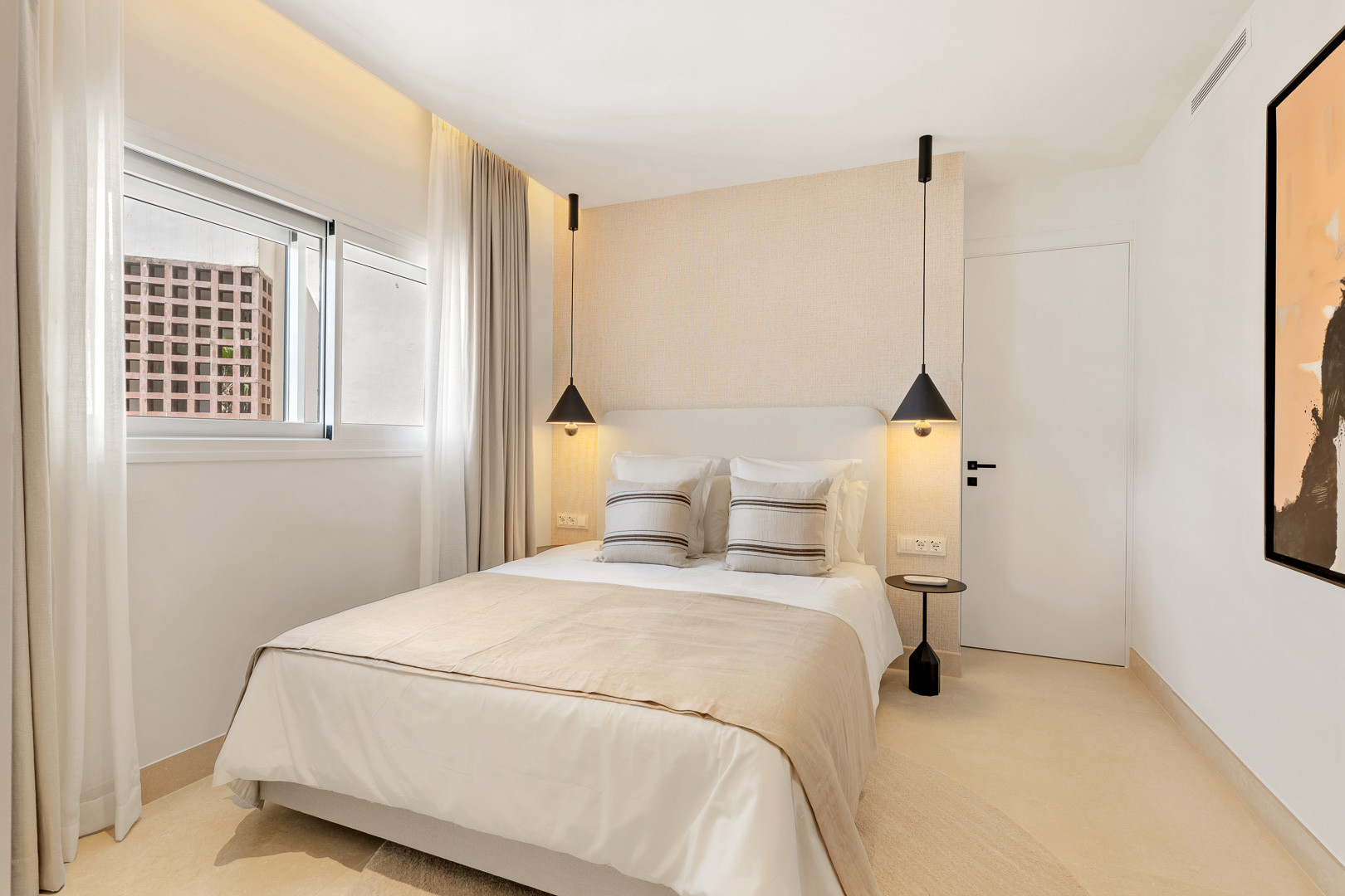 Bedroom with a queen-sized bed, two pendant lights, and a framed abstract artwork.