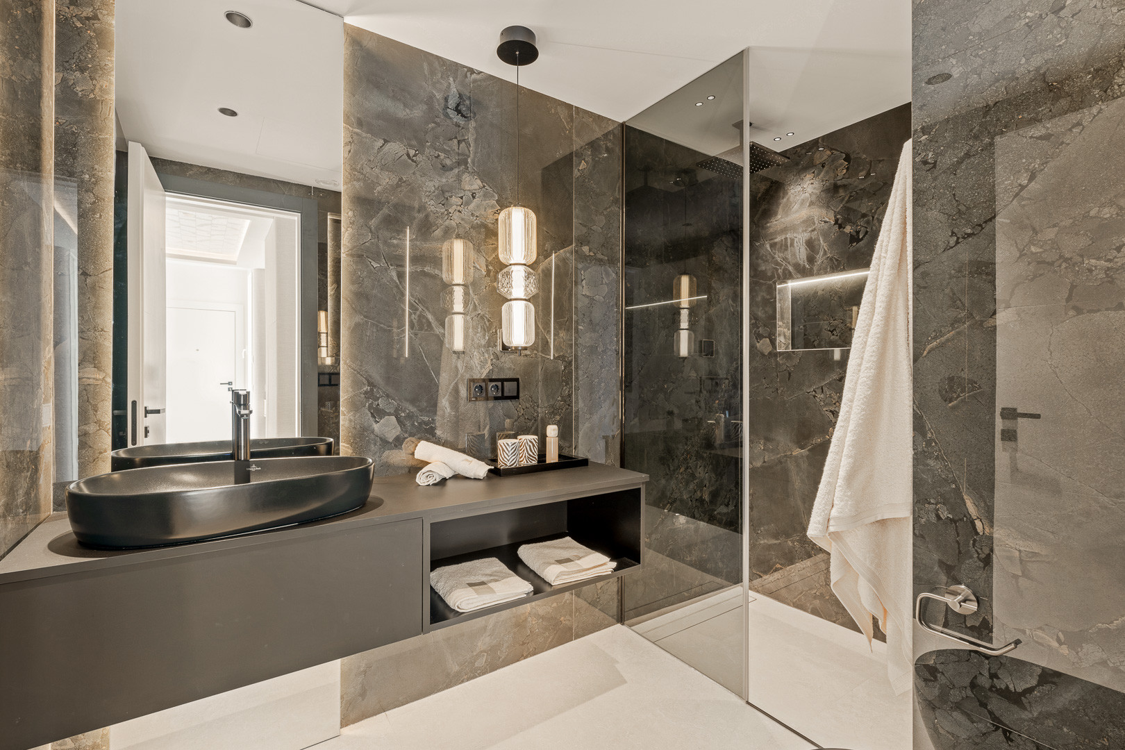 Modern bathroom with a dark oval sink on a floating vanity and large marble-patterned tiles.