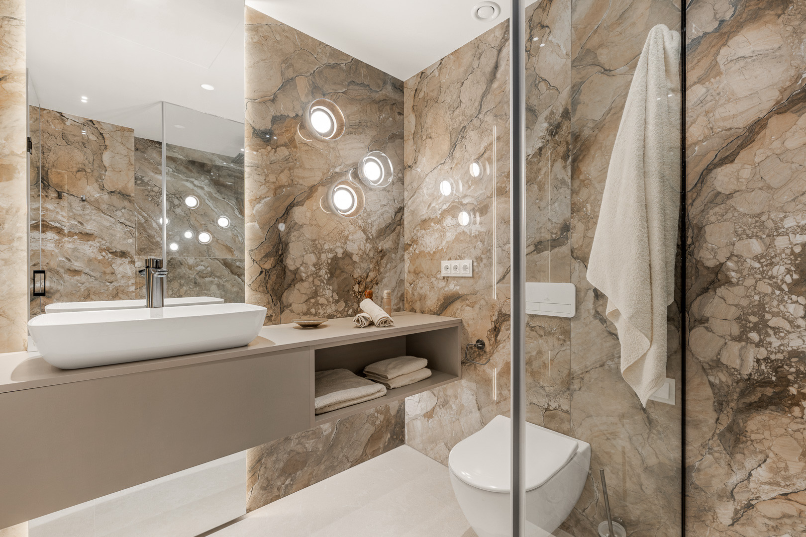 Bathroom with marble walls, modern vanity, white toilet, and circular wall lights.