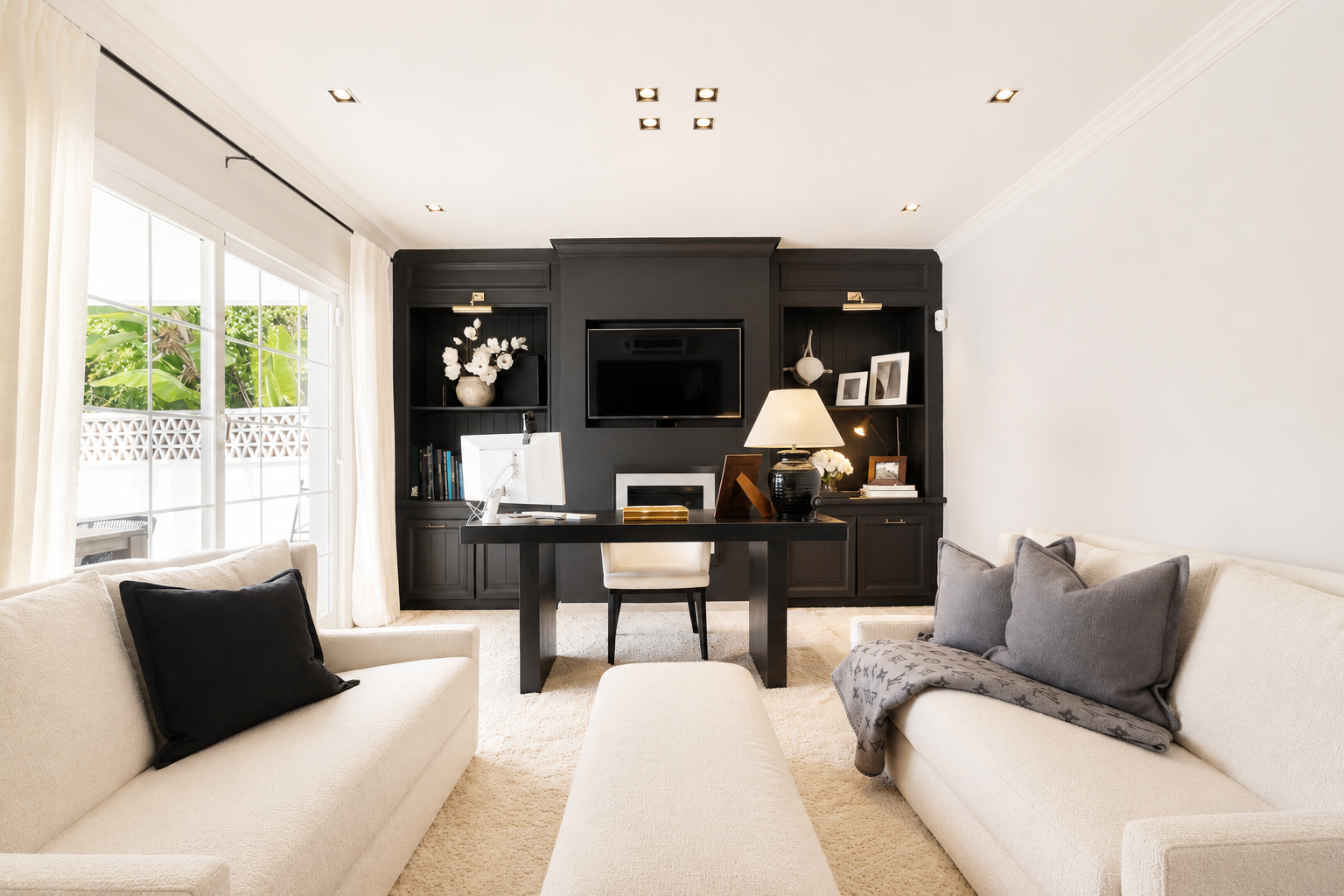 Cozy office space with a black desk, white chair, and built-in shelves, illuminated by natural light through curtains.