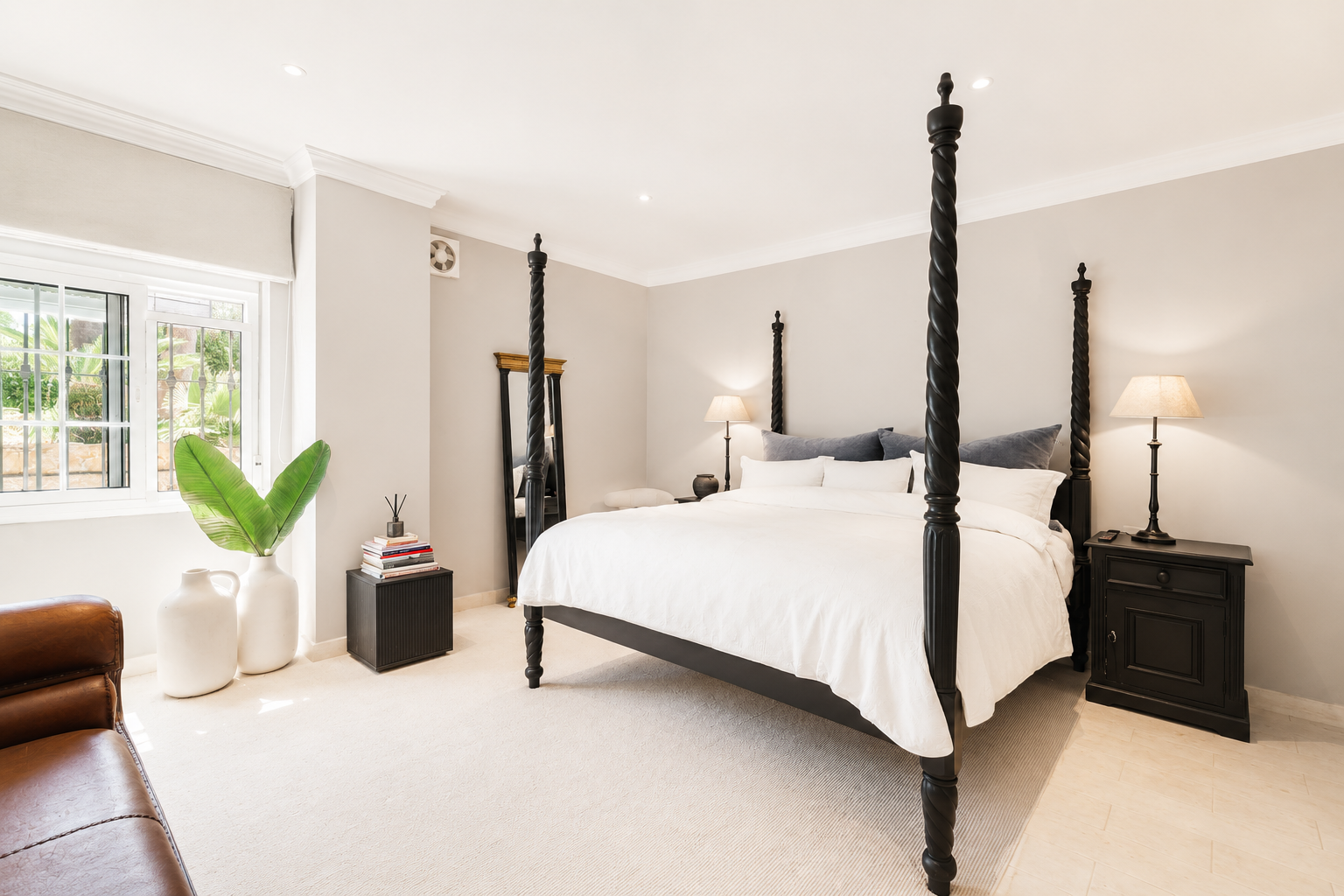 Elegant bedroom showcasing a four-poster bed, side table, and large window with greenery visible outside.