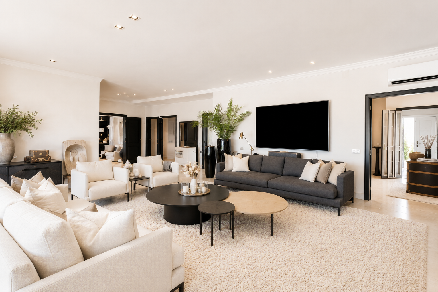 Spacious living room with a large grey sofa, cream chairs, and a decorative rug under a stylish coffee table.