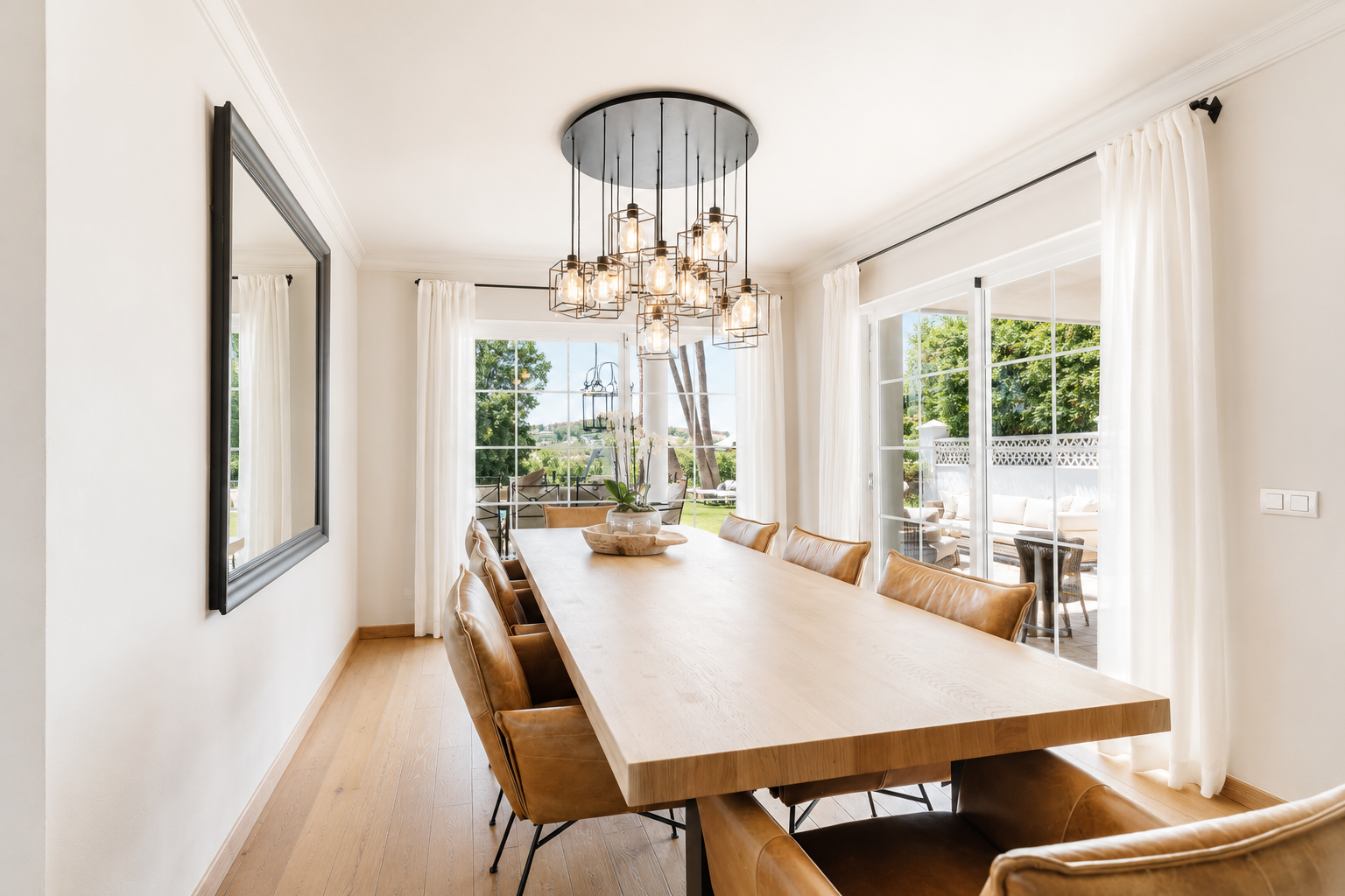 Bright dining area featuring a large table and modern light fixture, with outdoor view through sliding doors.