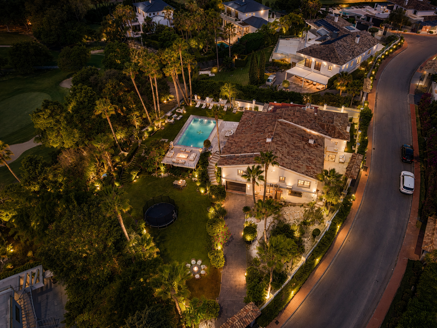 Aerial nighttime view of the villa surrounded by gardens, pool, and pathway lights illuminating the landscape.