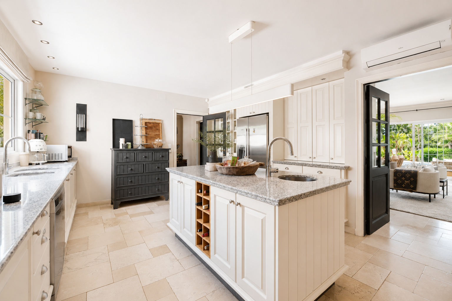 Modern kitchen with an island, gray granite countertops, and a glimpse into an adjacent living area.