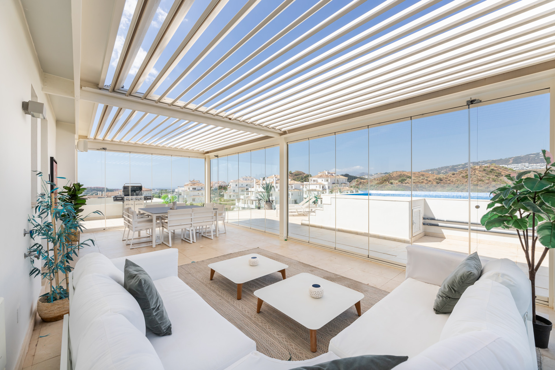 Modern sitting area with white furniture, dining table, and large glass windows for natural light.