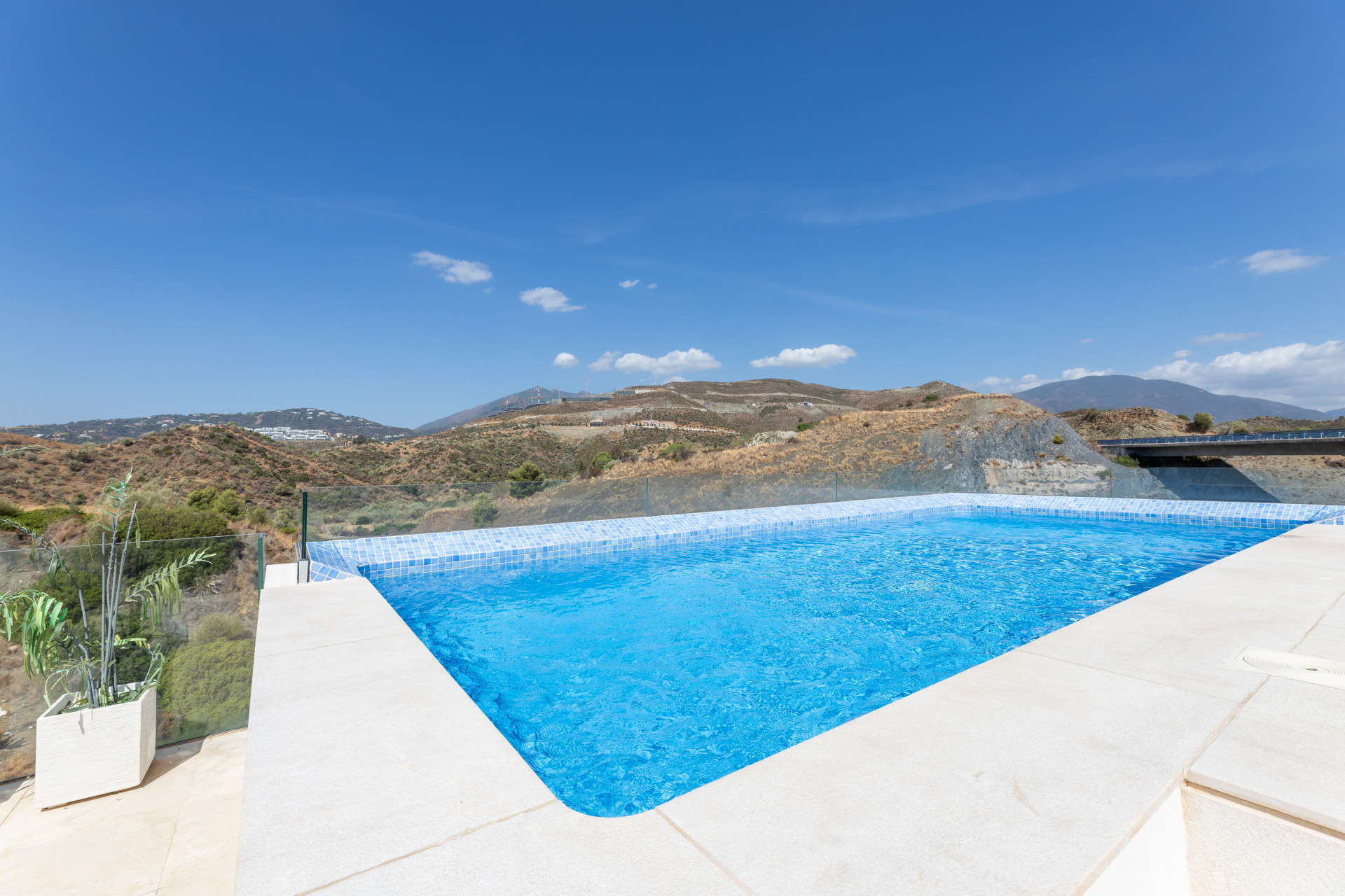 Infinity pool with clear blue water surrounded by rocky landscape and distant hills.