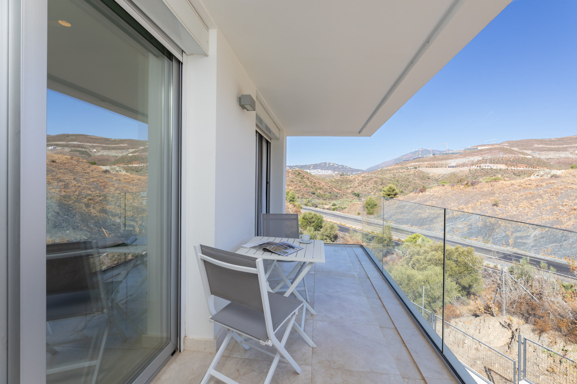 Balcony with a table and chairs overlooking natural scenery and mountains in the background.