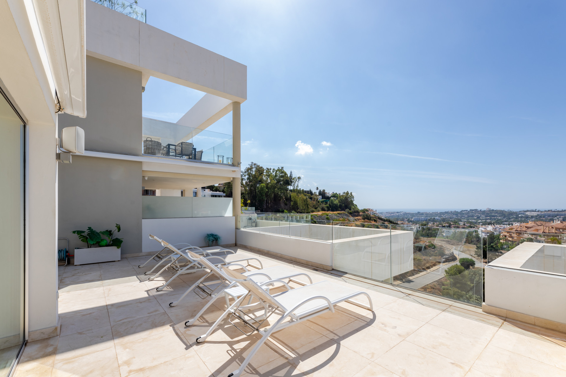 Spacious terrace with sun loungers and glass railing overlooking a hillside view in Marbella.