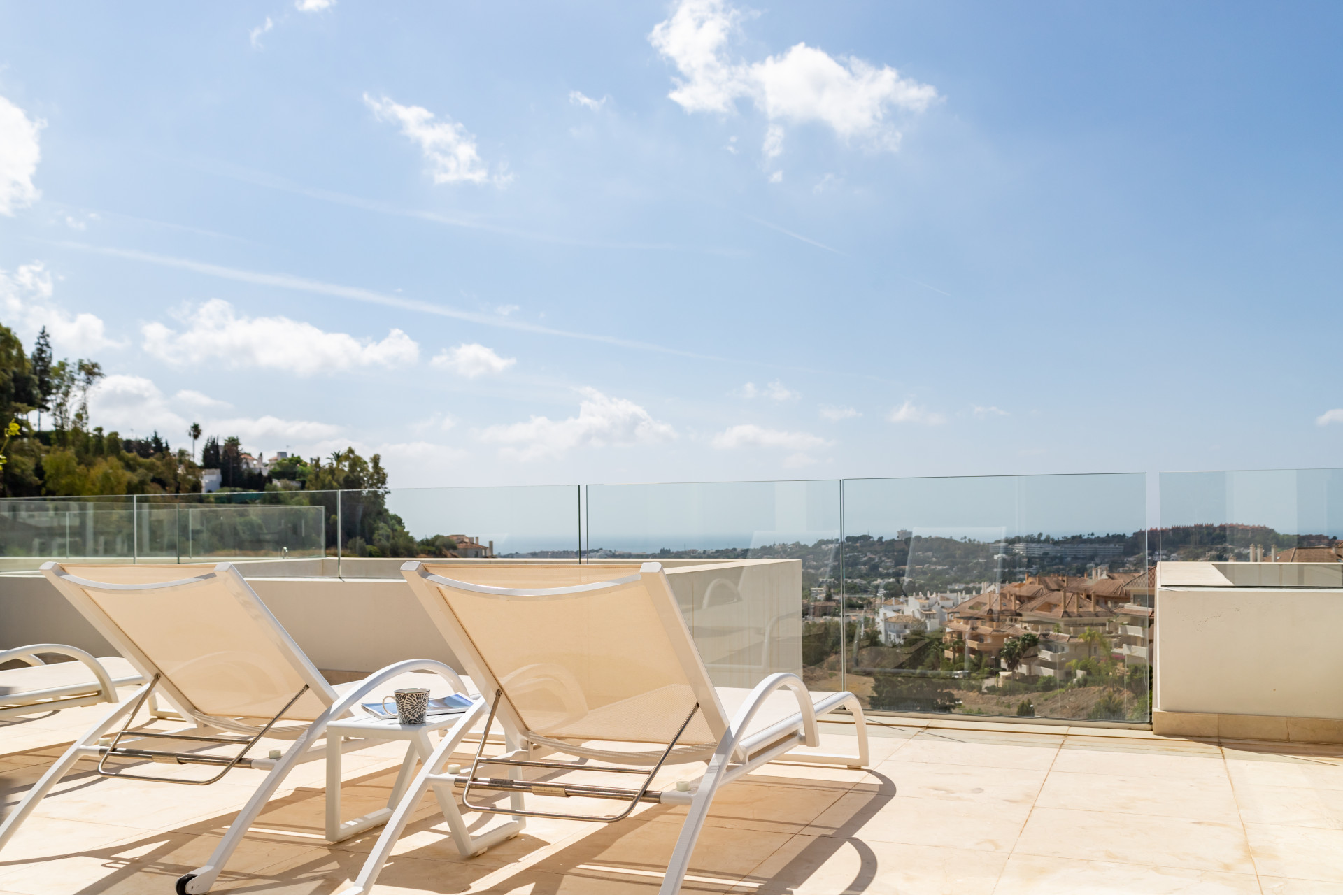 View of the terrace with lounge chairs overlooking a coastal landscape under a blue sky.