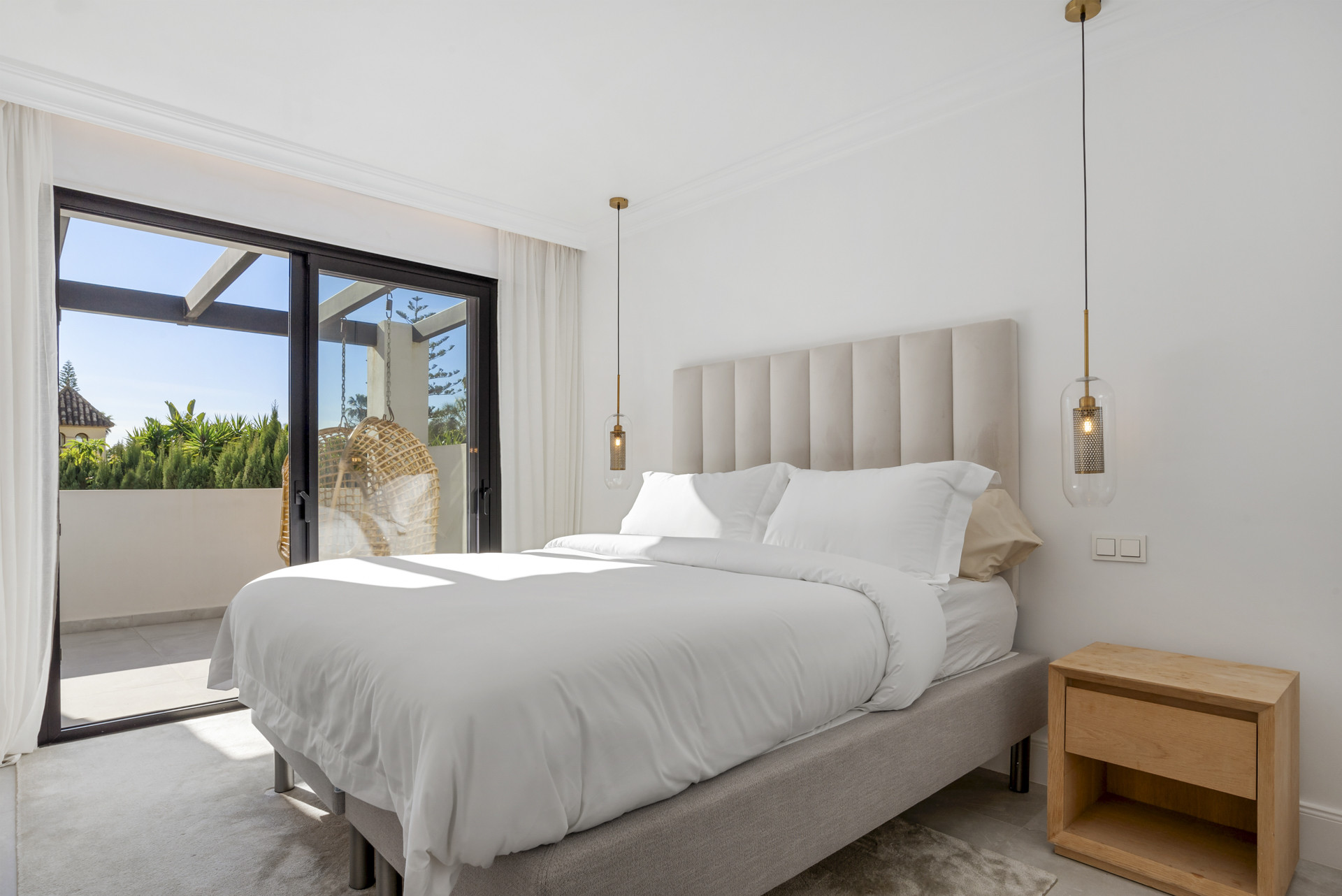 Bright bedroom with large window, white bedding, and pendant light above the bed.