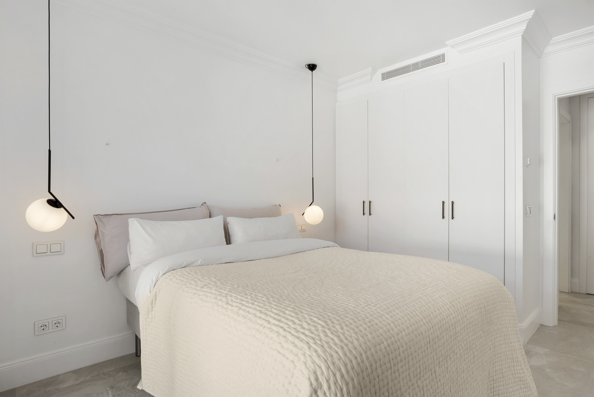 Serene bedroom with a textured blanket, pendant lights, and built-in wardrobe.