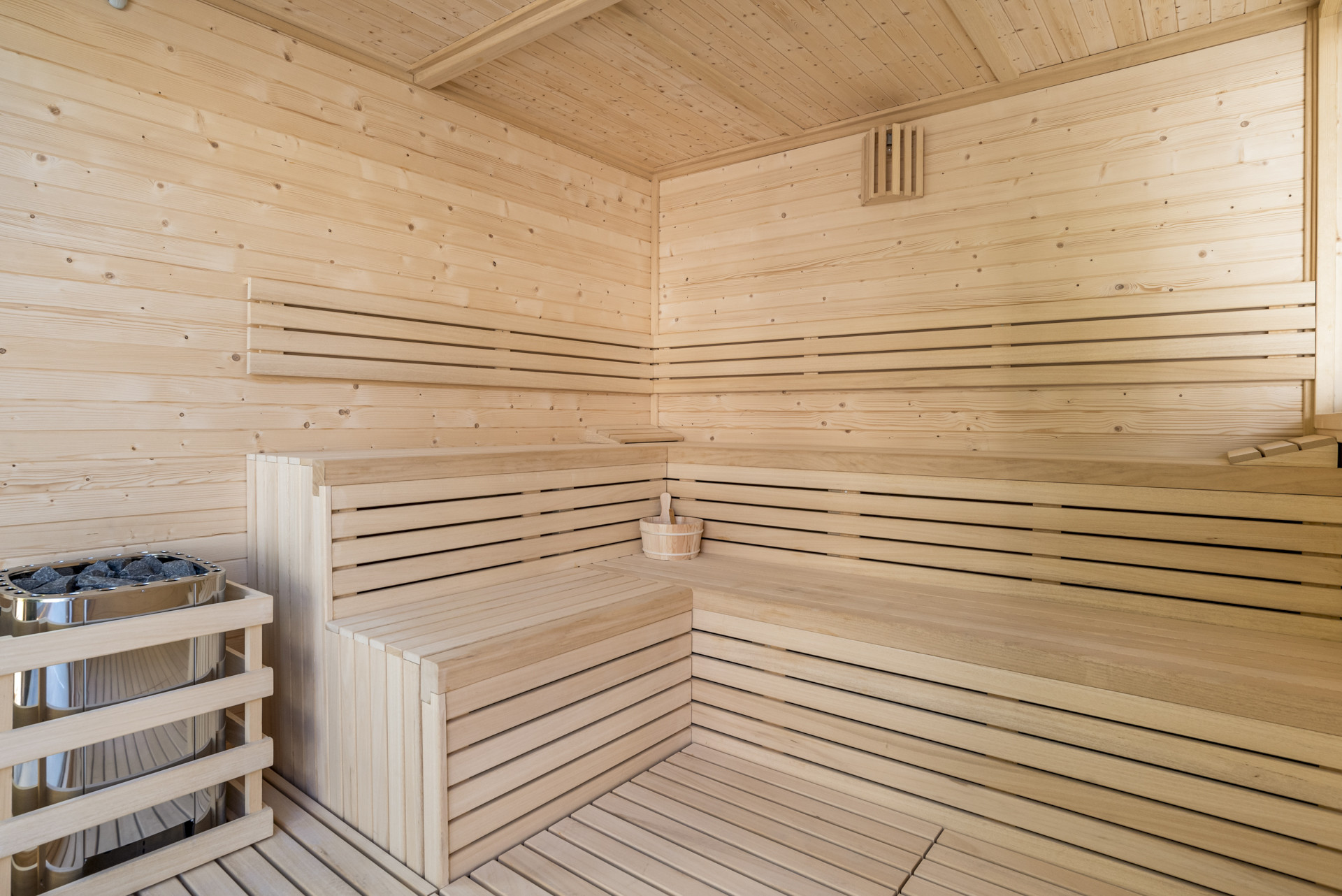 Interior of the sauna featuring wooden benches and a heater with stones, creating a warm atmosphere.