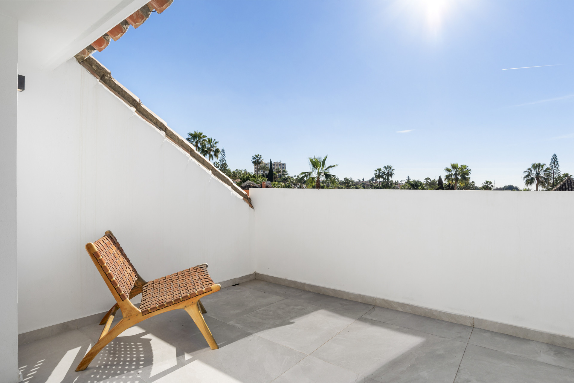 Private balcony with a single wooden chair and sunny sky